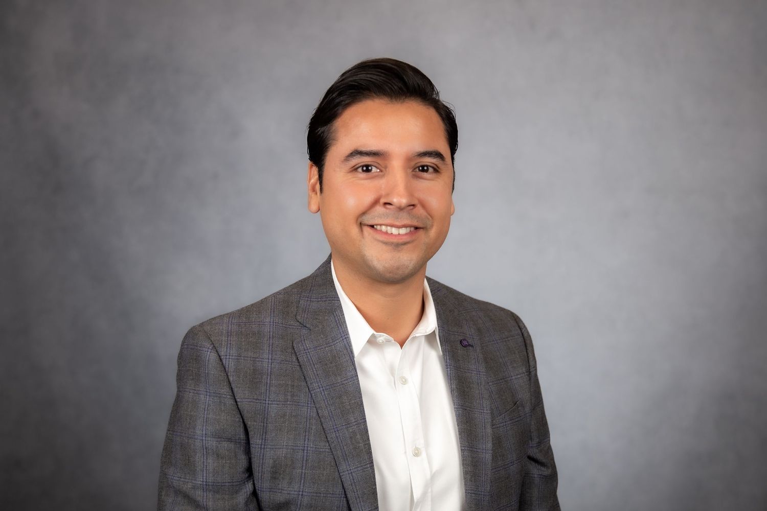Smiling professional man in gray suit jacket on a gray studio background.