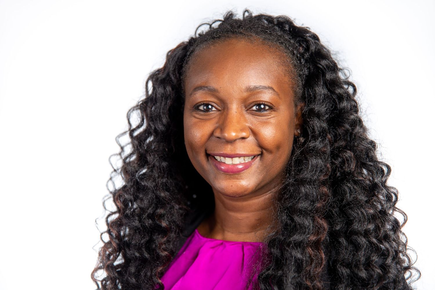 Smiling Black woman with curly hair wearing pink top against white background.