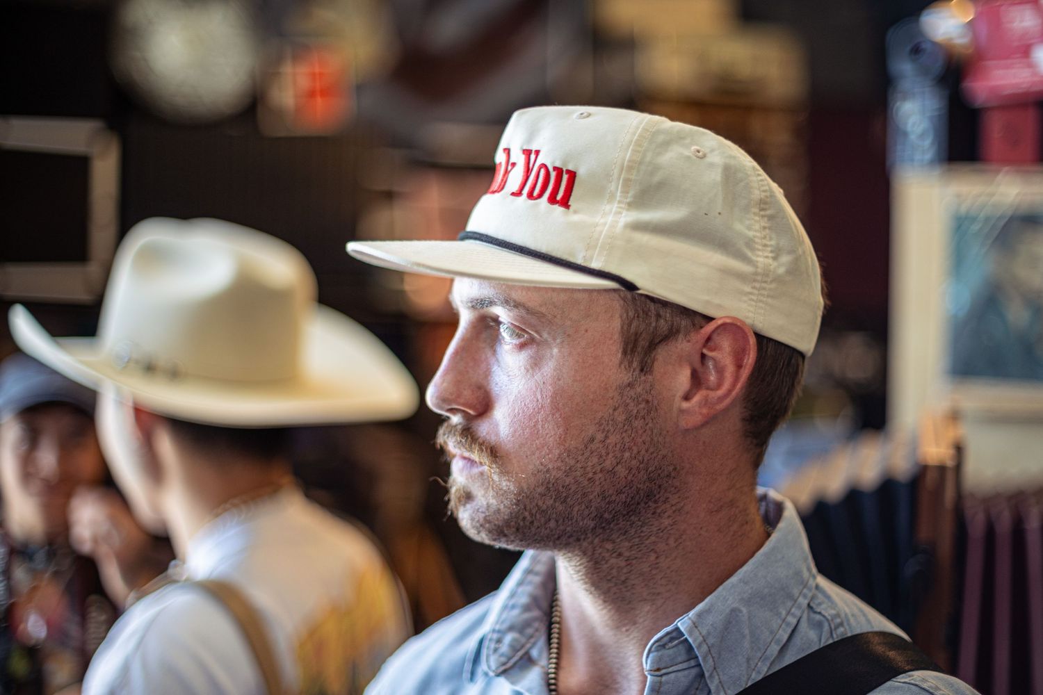 Man wearing a vintage cream baseball cap browsing hats in a western clothing store.
