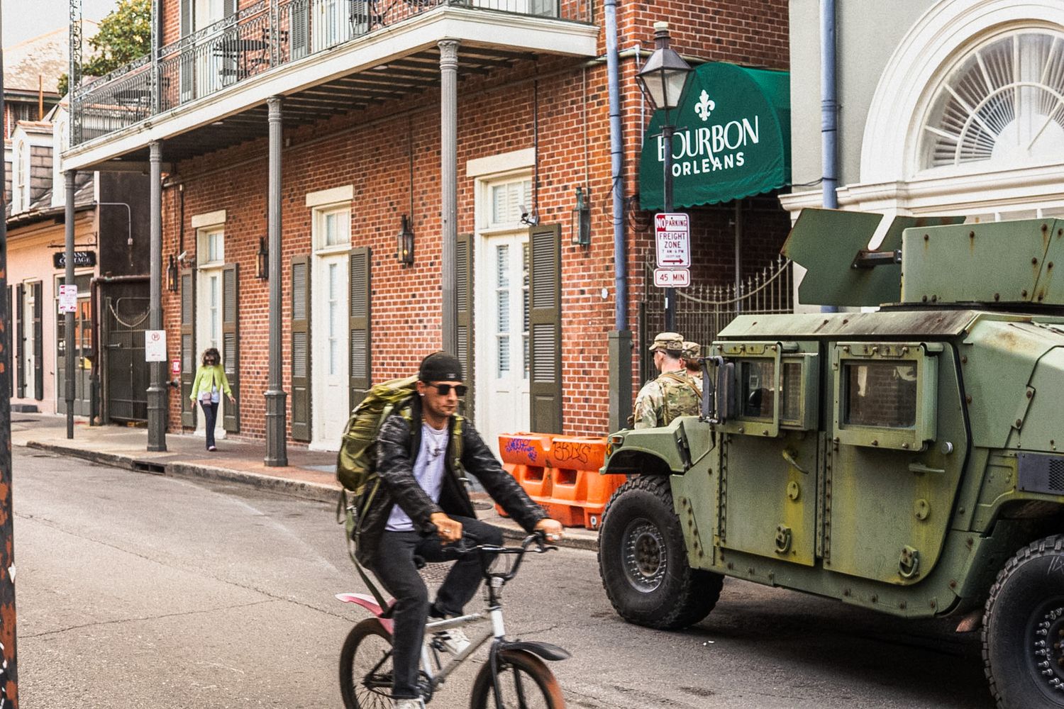 Cyclist riding past a military Humvee on a New Orleans French Quarter street near a Bourbon Orleans sign.