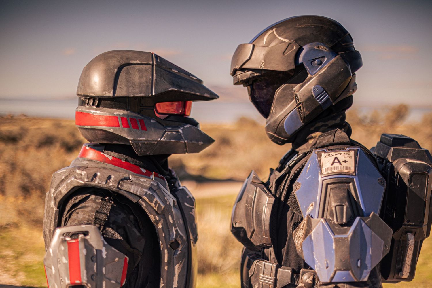 Two people in detailed Halo ODST cosplay armor face each other outdoors in a desert landscape.