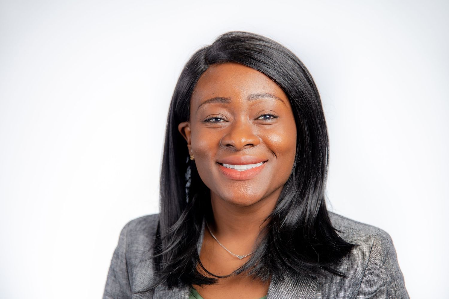 Professional headshot of smiling woman with straight black hair wearing gray blazer on white background.