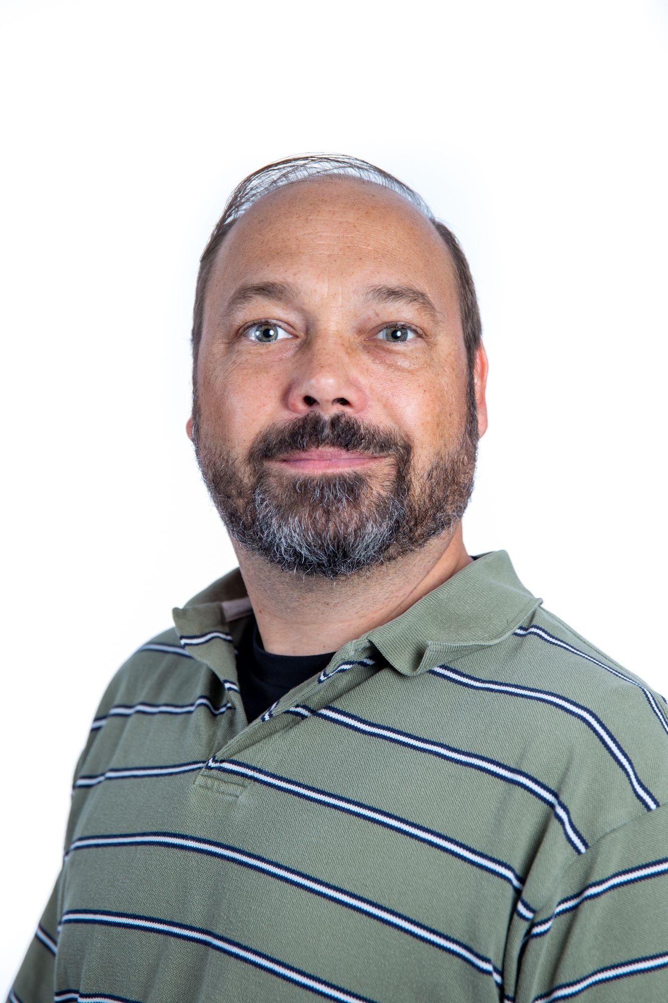 Bearded man wearing kippah in striped polo shirt poses for headshot on white background.