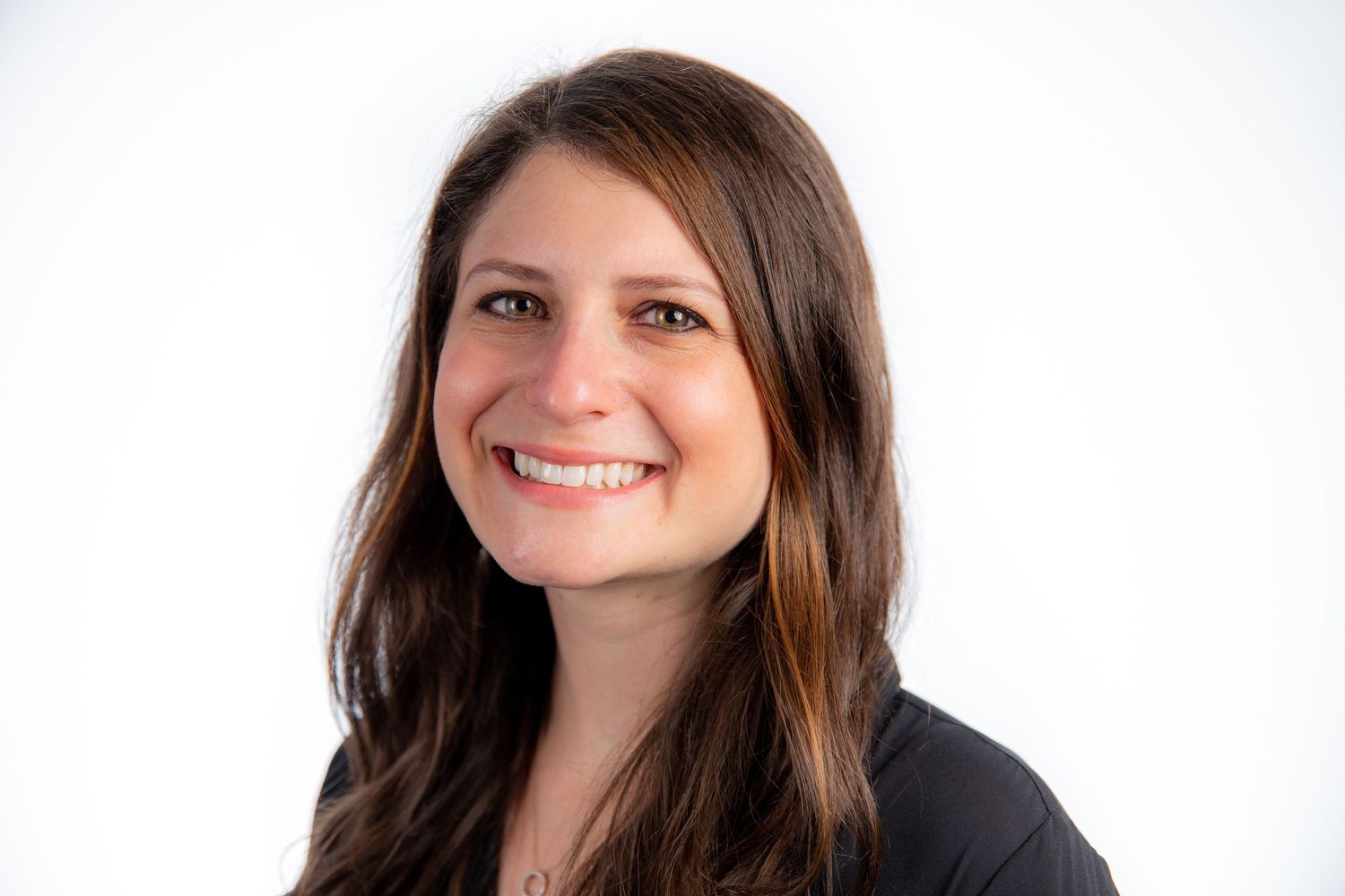 Smiling young woman with long brown hair wearing a black top against a white background.