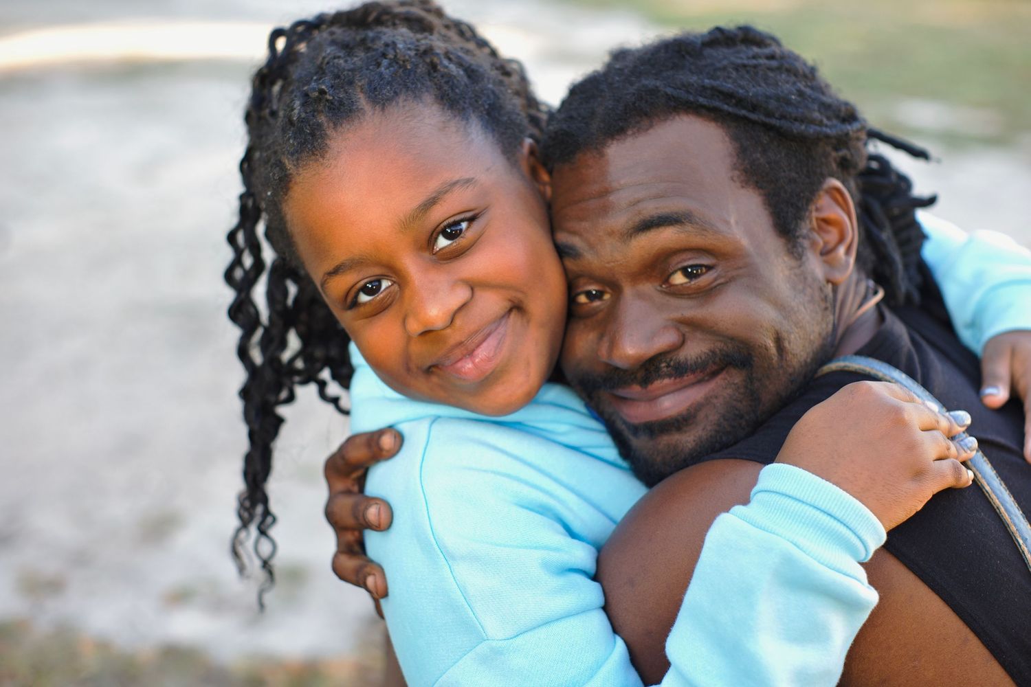 Smiling man with locks hugging girl outdoors in warm embrace.