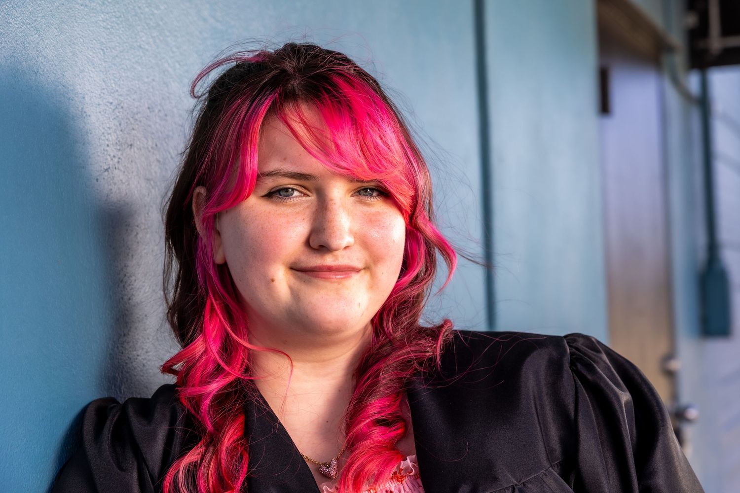 Young woman with vibrant pink hair smiling warmly in a close-up outdoor portrait.