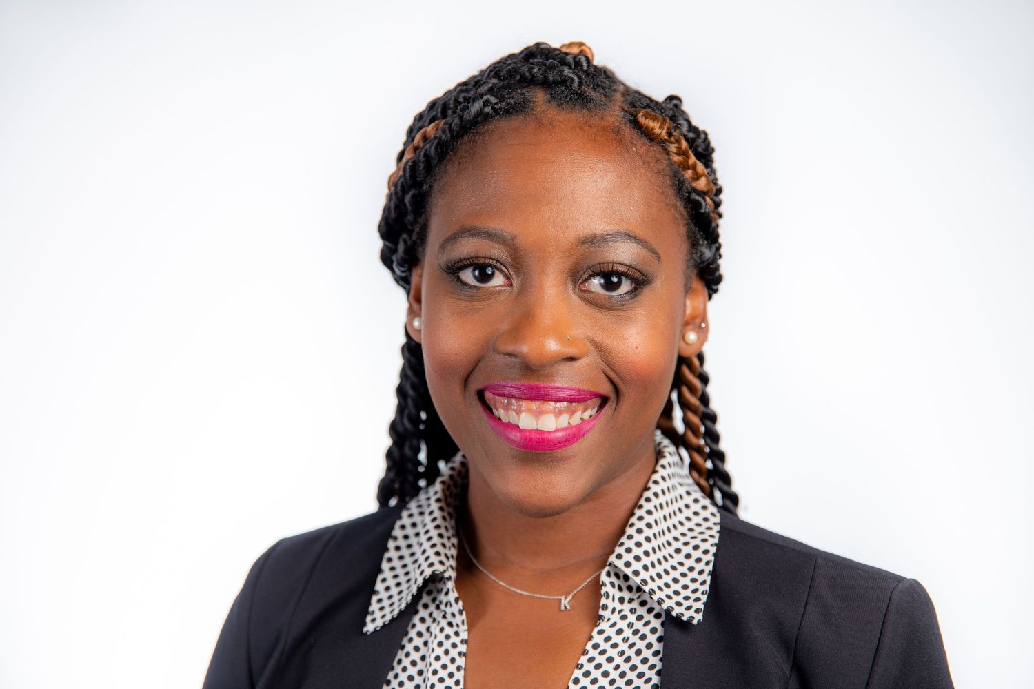 Smiling woman with braided hair wearing a black blazer and pink lipstick.