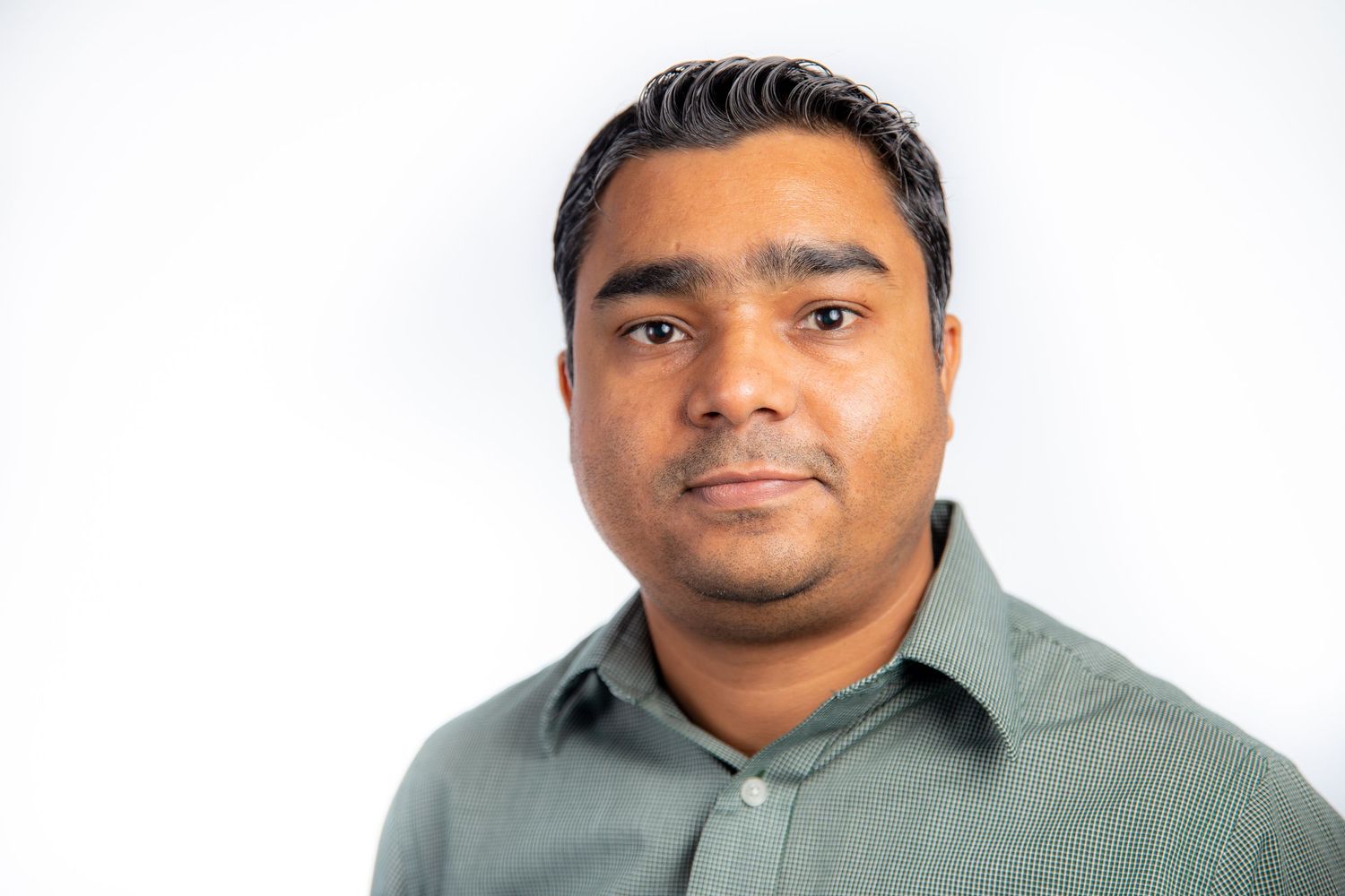 Professional man in gray button-up shirt posing for headshot against white background.