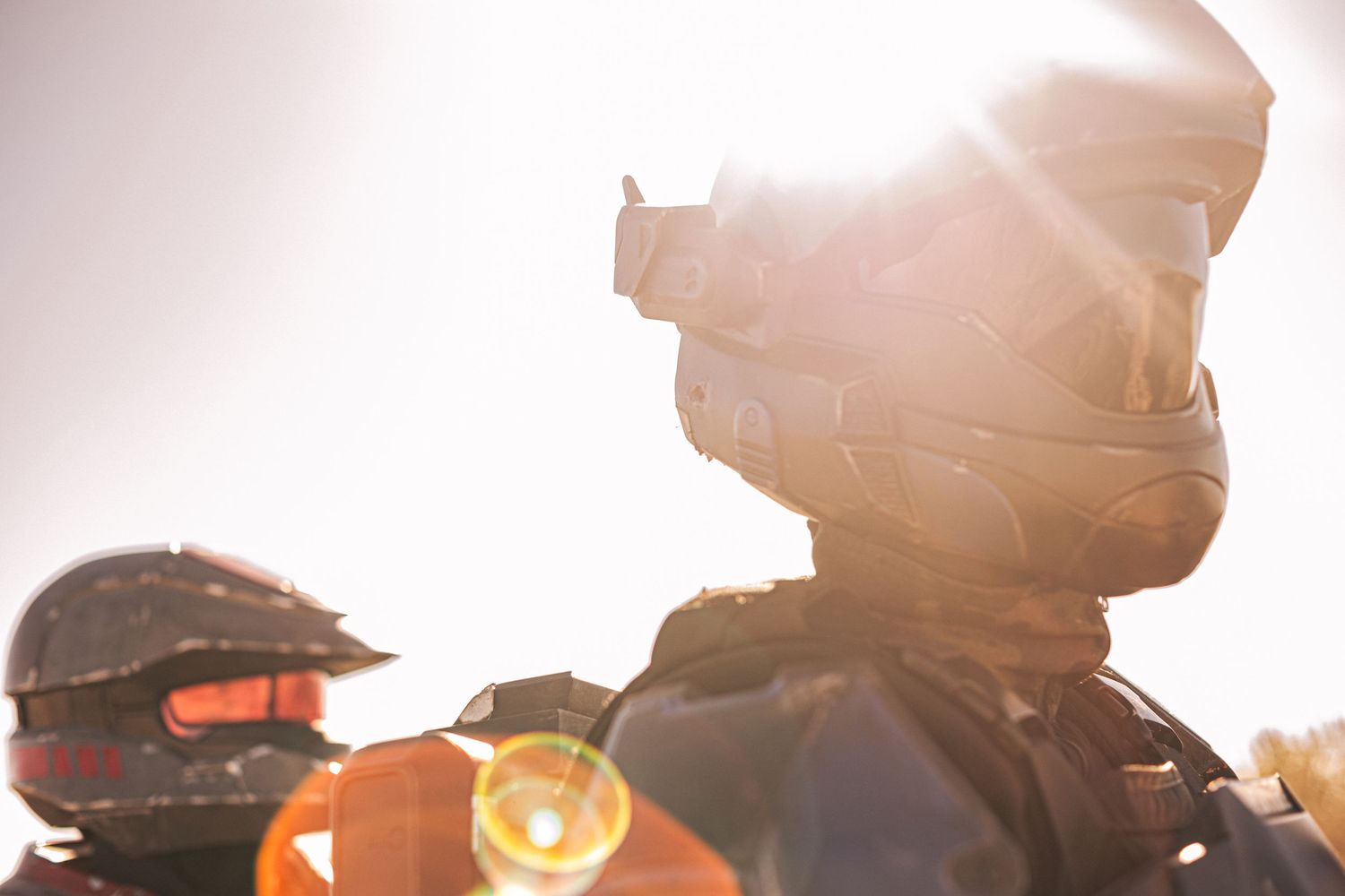 Two soldiers in tactical helmets and gear silhouetted against a bright sunlit sky outdoors.
