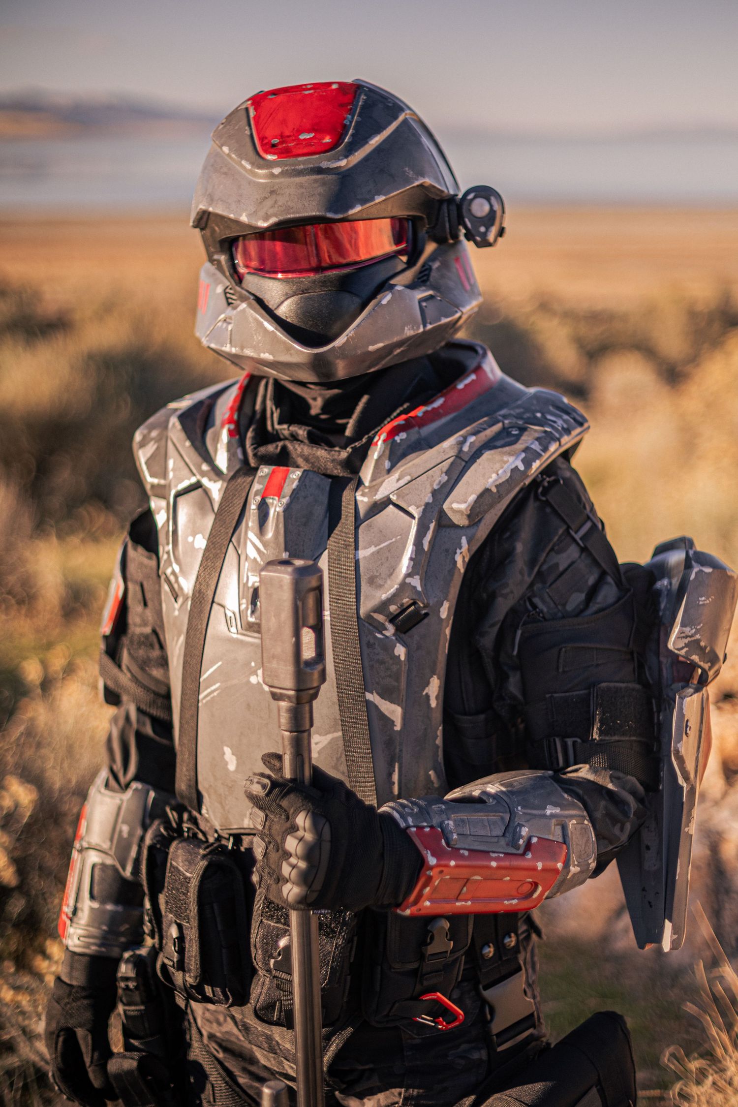 Person in detailed black and red futuristic combat armor standing in desert scrubland.