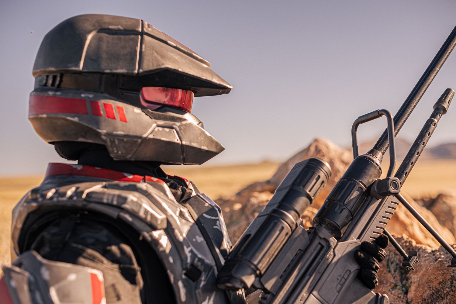 Futuristic soldier in sci-fi armor and helmet holding a rifle in a desert landscape.