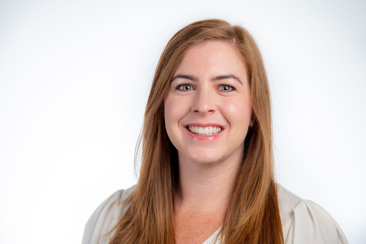 Smiling woman with long red hair wearing a white blouse against a white background.