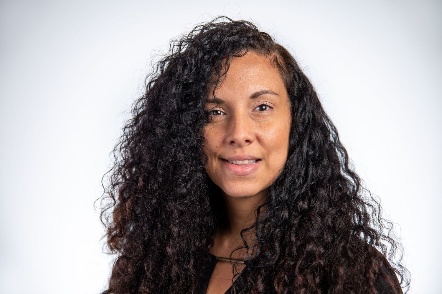 Woman with long curly dark hair smiling softly against a white background.