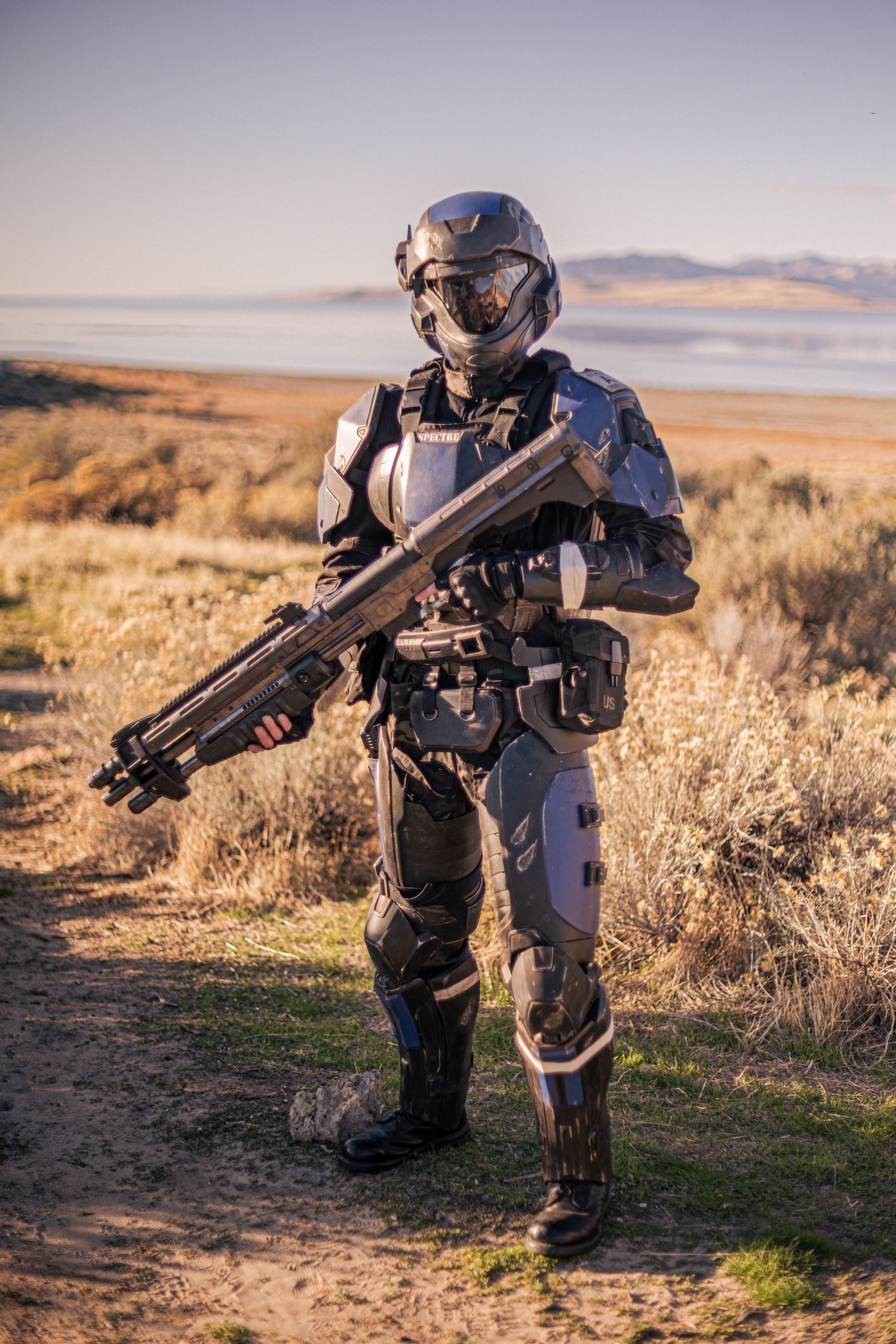 Person in detailed futuristic military armor holding a large sci-fi rifle in an arid outdoor setting.
