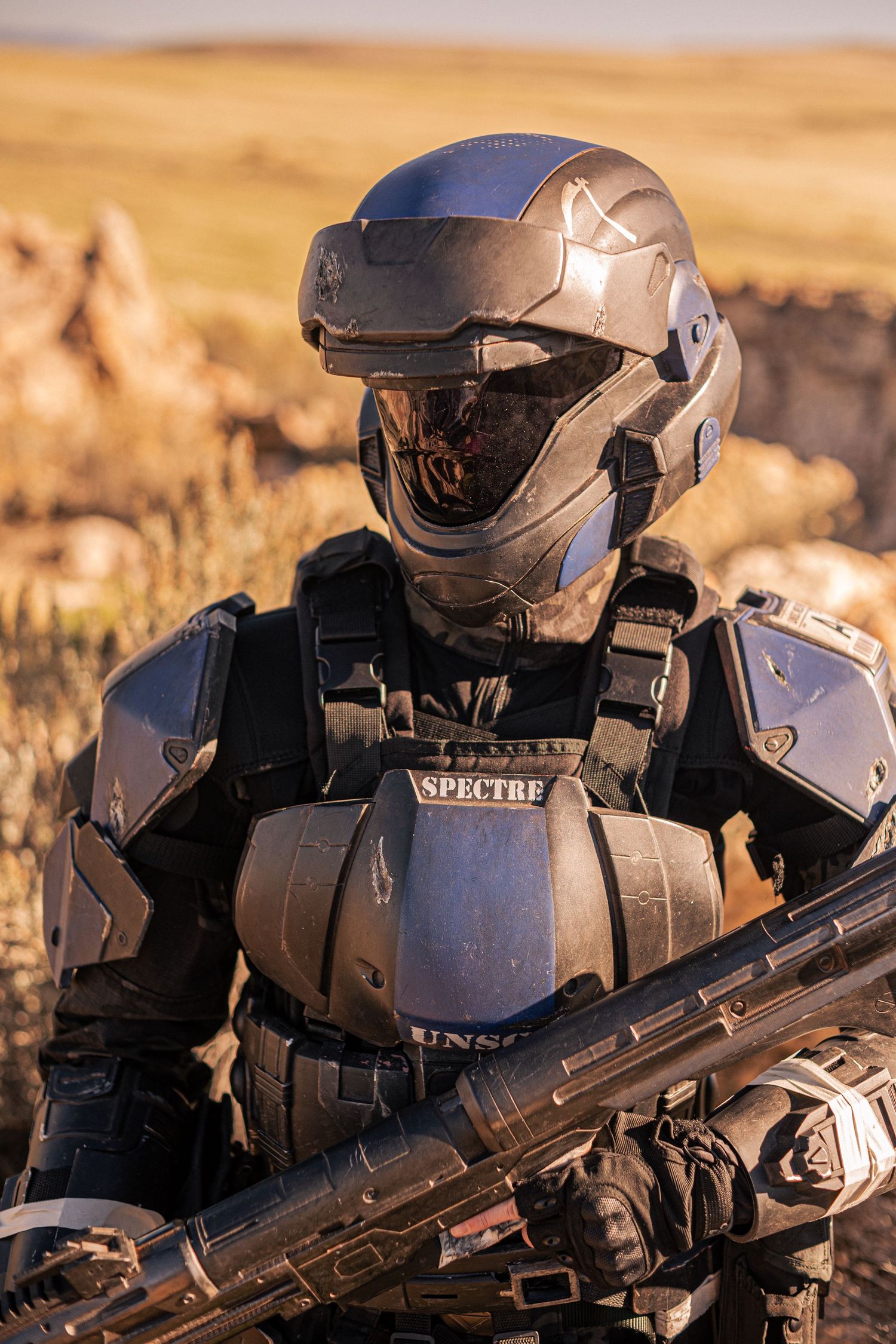 Person in detailed sci-fi SPECTRE UNSC combat armor holding futuristic weapon in desert setting.