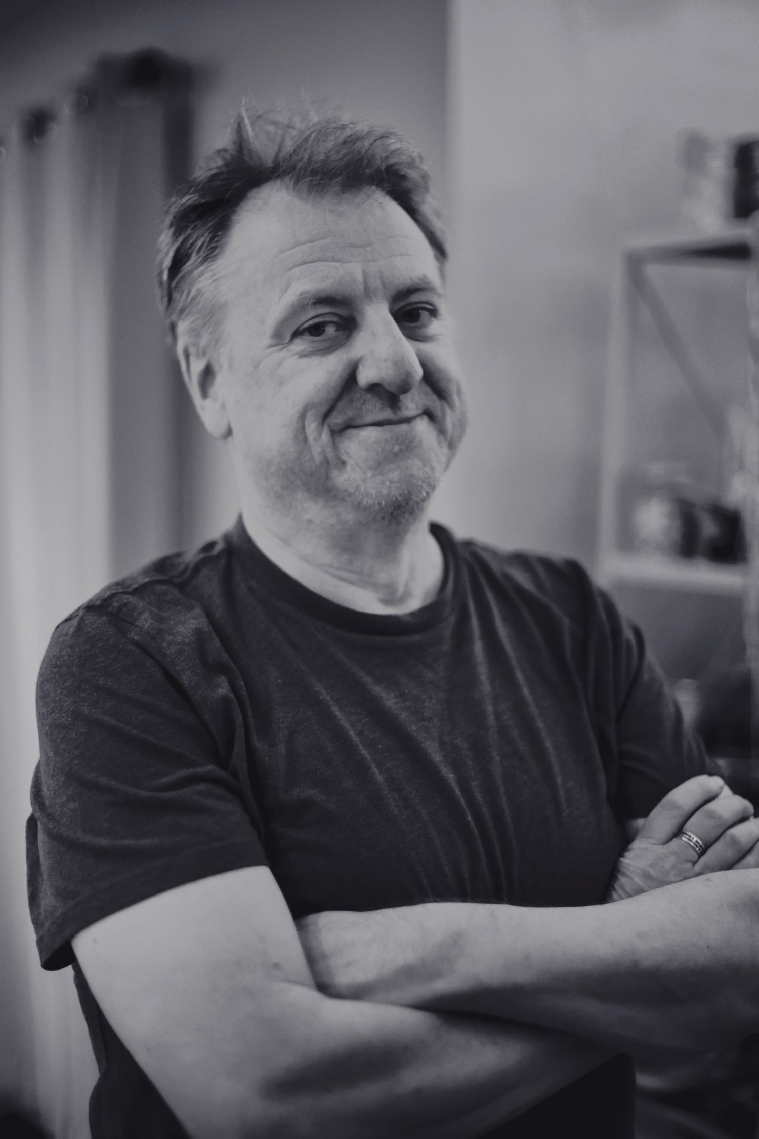 Black and white portrait of a middle-aged man with crossed arms smiling indoors.