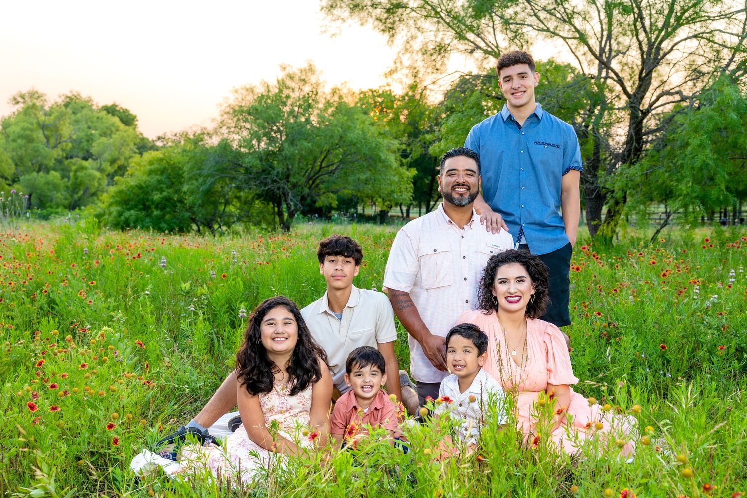 Family of seven posing in a wildflower meadow at golden hour with lush green trees in background.