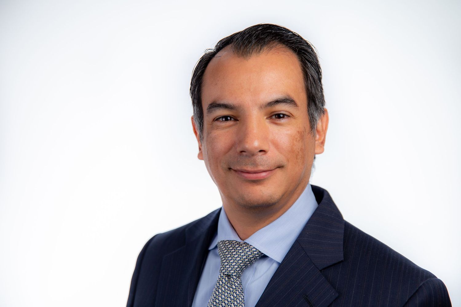 Professional man in a navy suit and tie smiling against a white background.