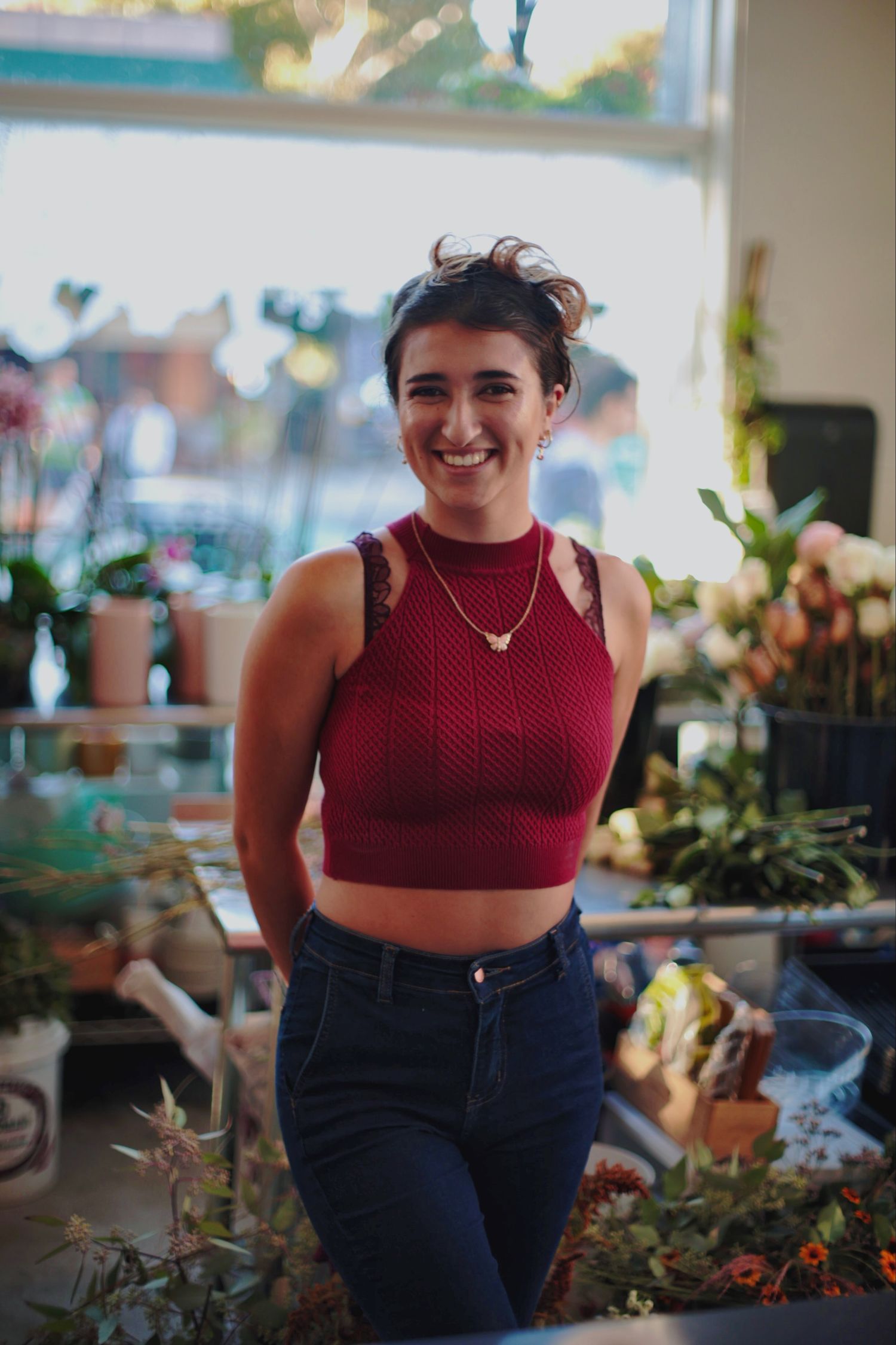 Happy young woman in a red crop top and jeans smiling in a flower shop surrounded by plants.