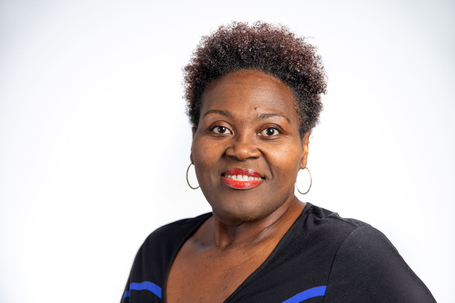 Smiling woman with short natural hair wearing black top and hoop earrings on white background.