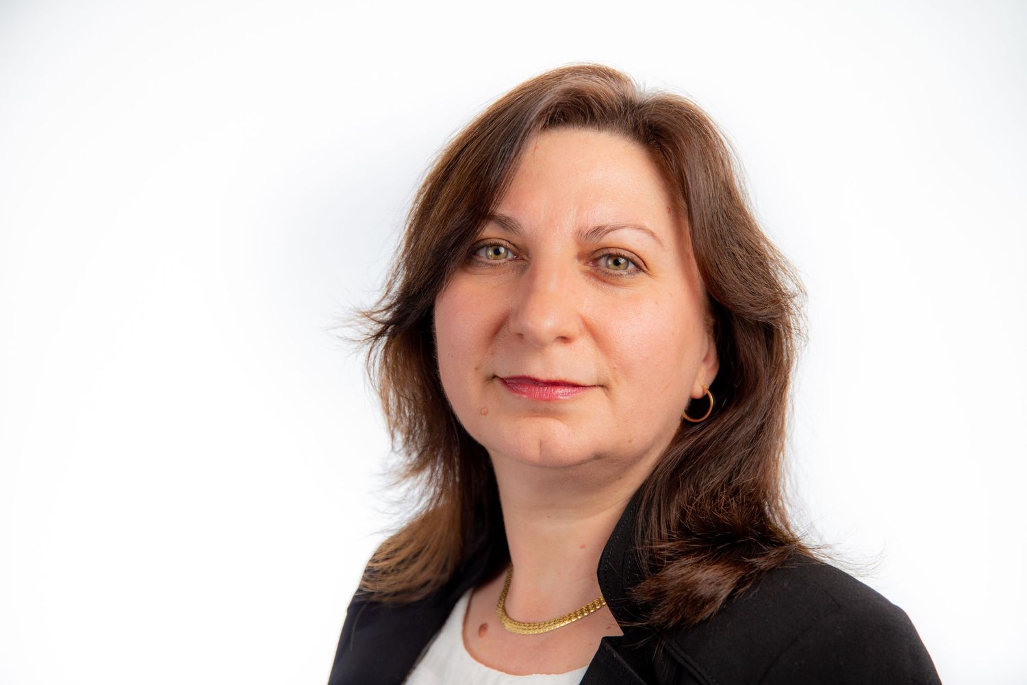 Professional headshot of a woman with brown hair wearing a black blazer and gold necklace against a white background.