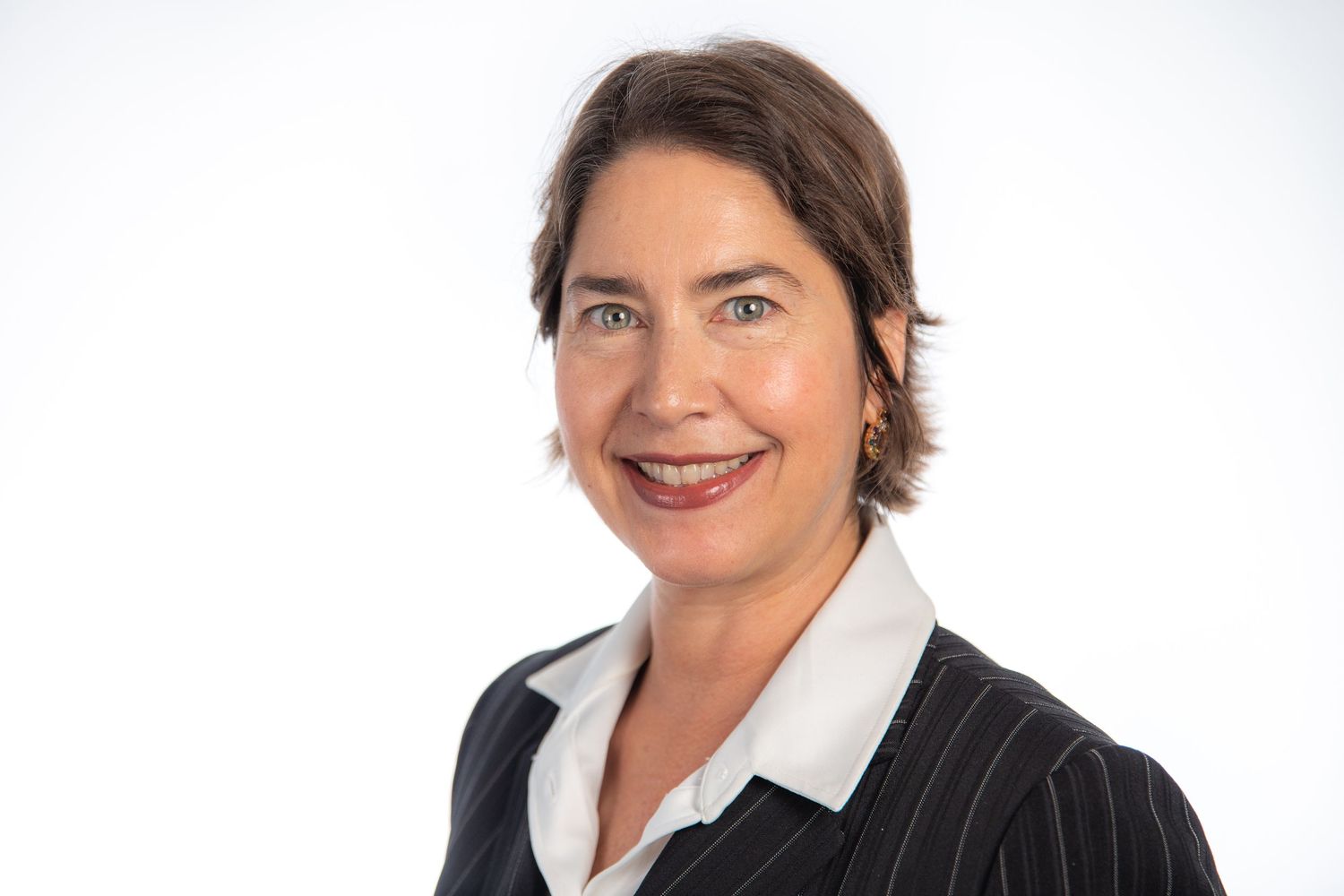 Professional woman with brown hair wearing a pinstripe blazer, smiling headshot on white background.