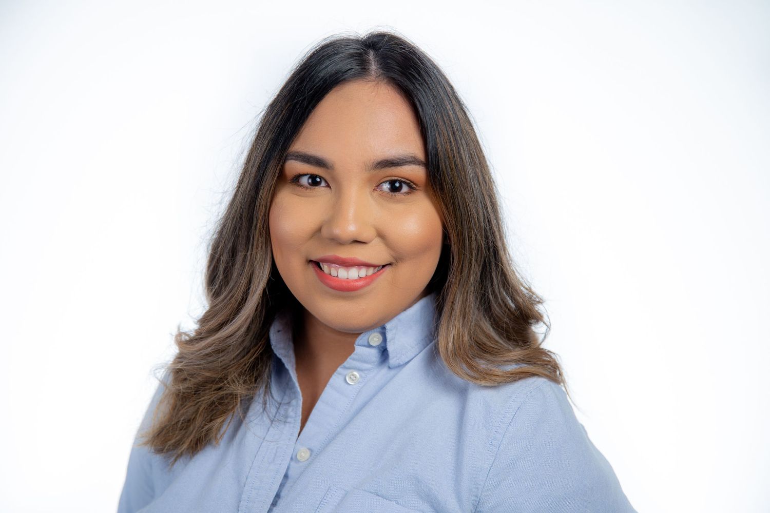 Young Latina woman smiling in light blue shirt against white background.