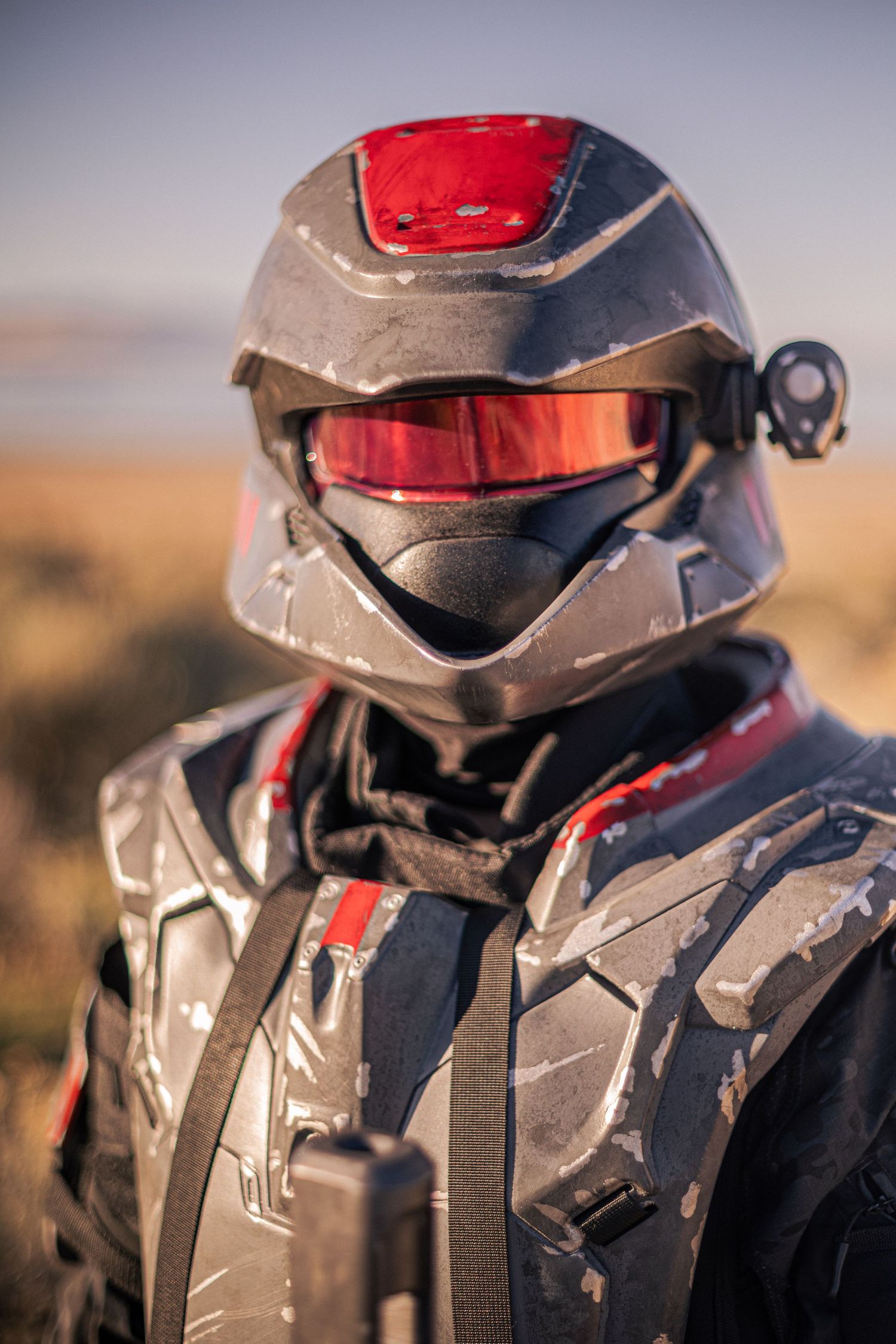 Person in detailed black and red sci-fi combat armor helmet with red visor outdoors.