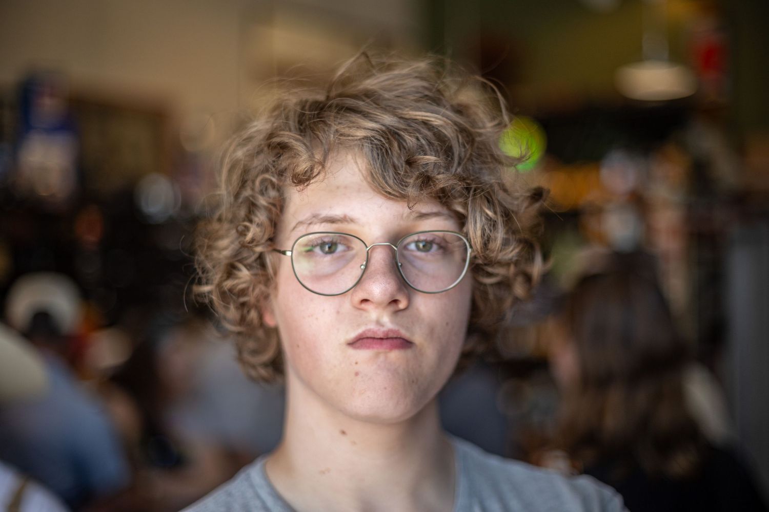 Teenage boy with curly hair and glasses in casual portrait setting.