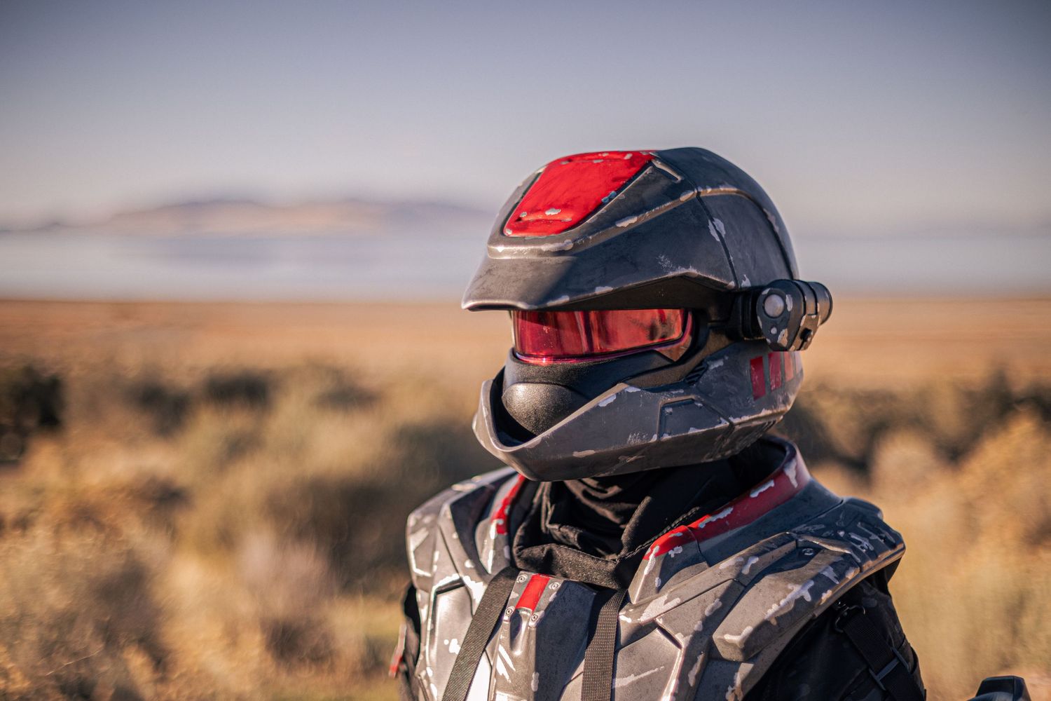 Close-up of soldier wearing dark tactical armor with red-visor helmet in desert setting.