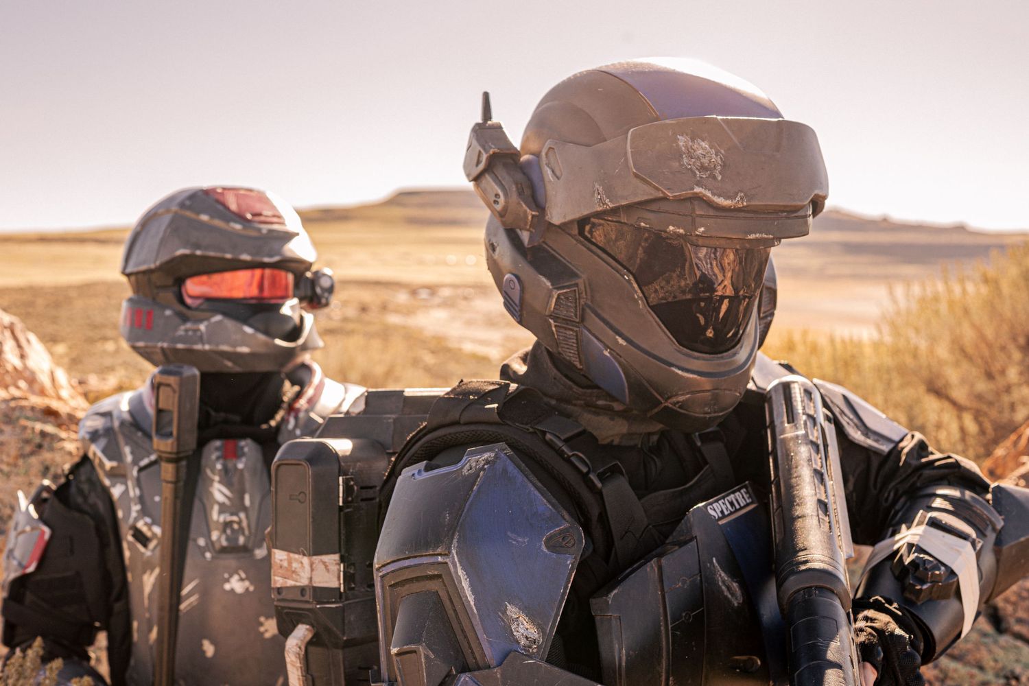 Two cosplayers in detailed futuristic military armor helmets in arid outdoor setting.