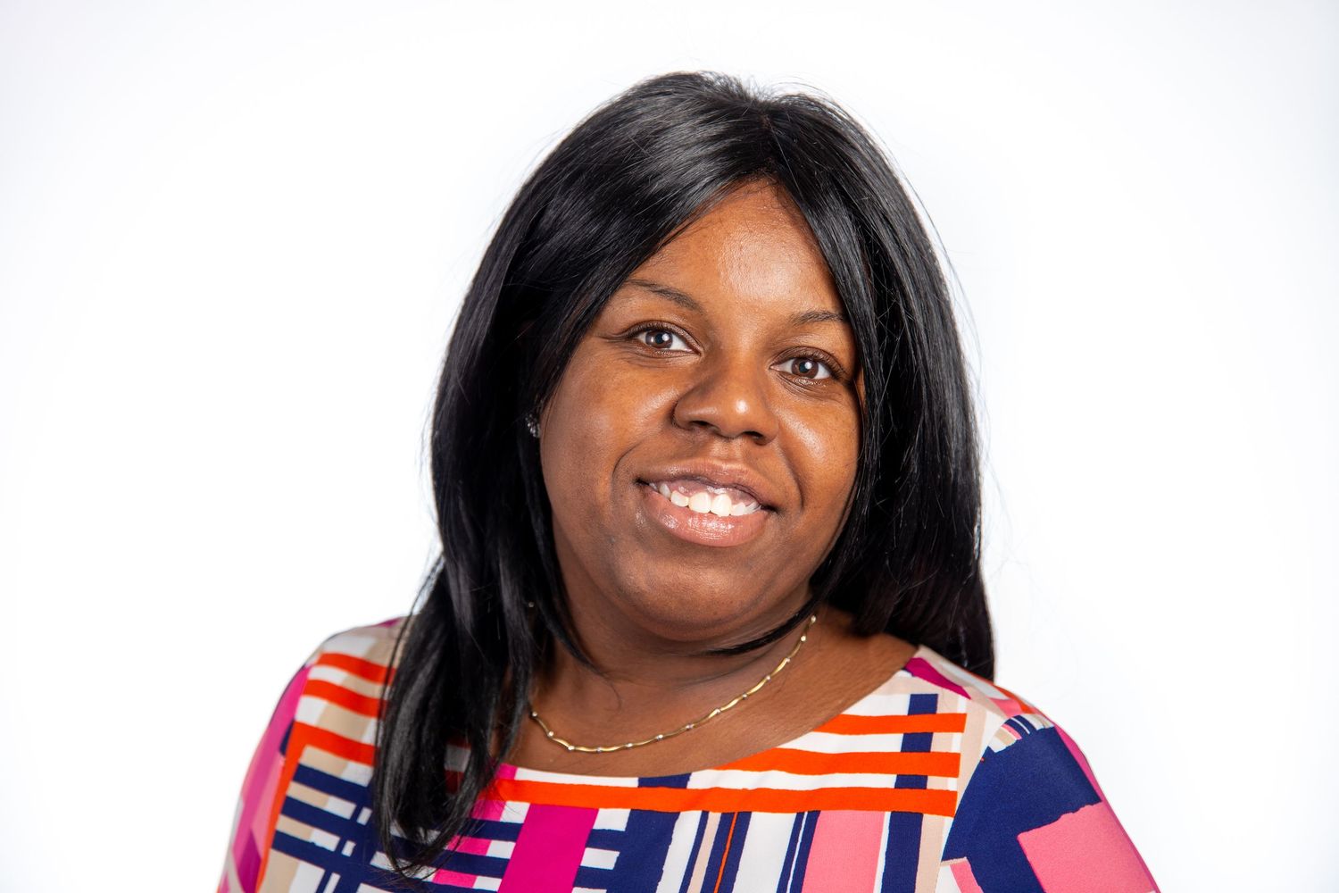 Smiling woman in a colorful striped top wearing a gold necklace poses for a professional headshot.