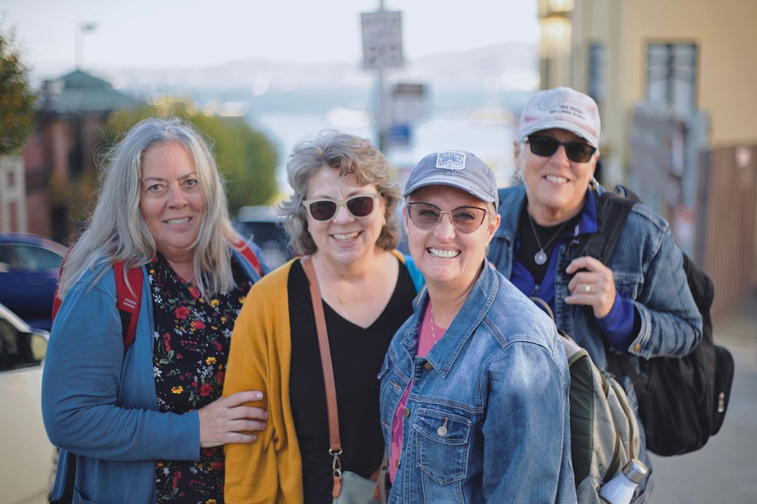 Four smiling women pose together outdoors on a city street at dusk.