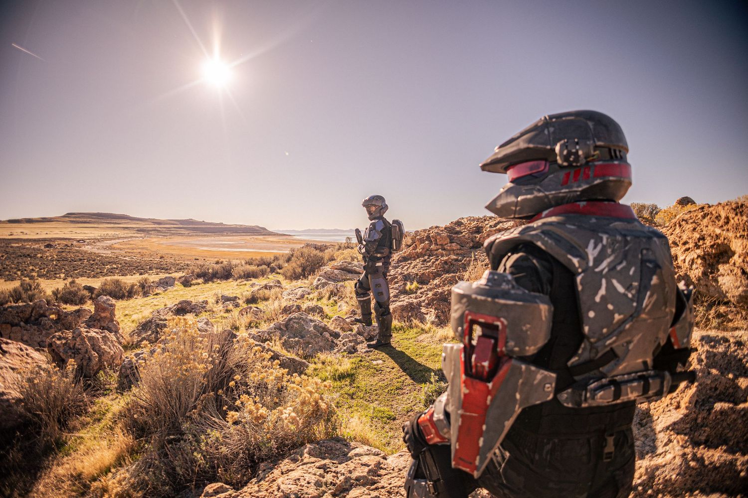 Two people in sci-fi combat armor surveying vast desert landscape under bright sun.