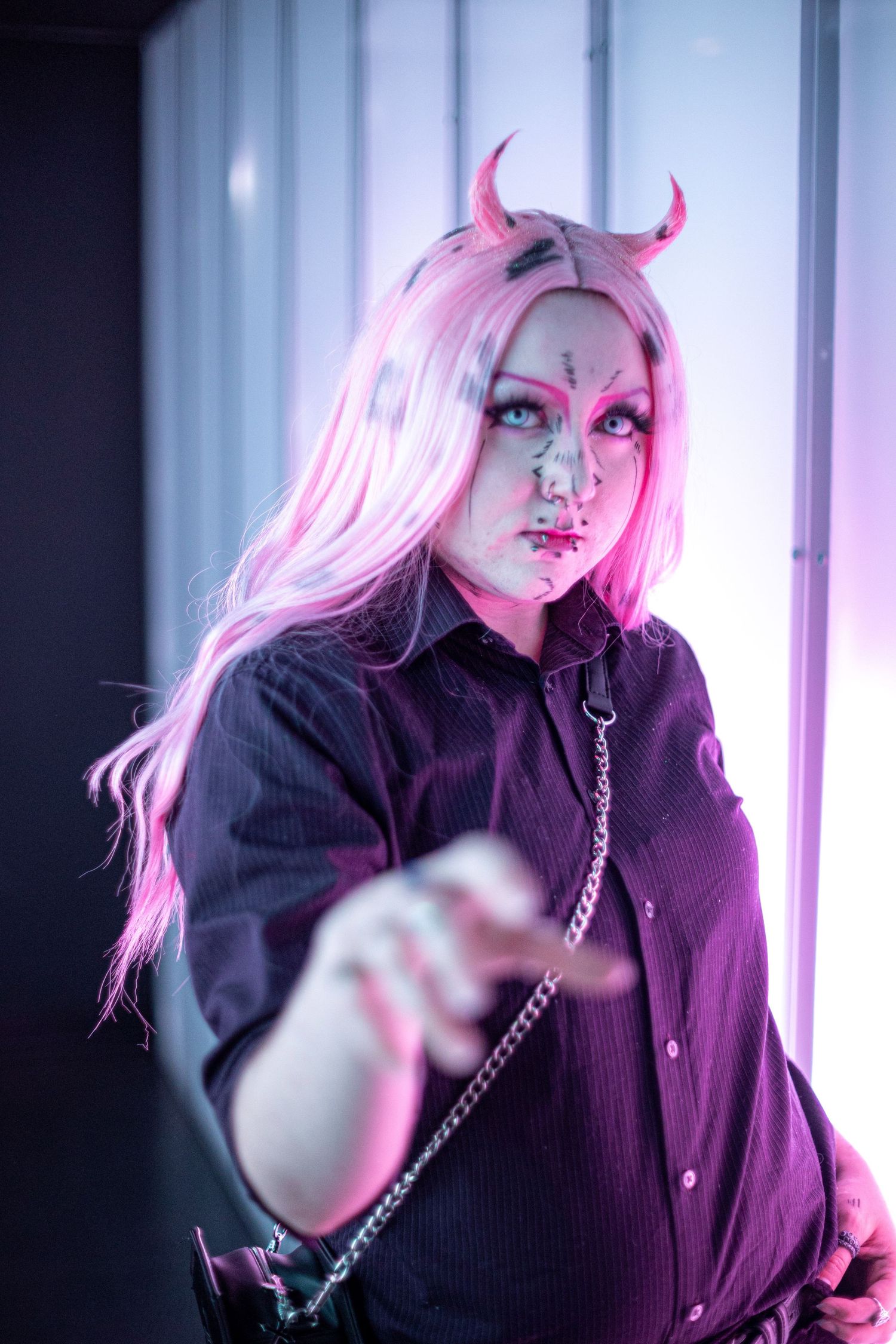 Person in demon cosplay with pink hair and horns reaching toward camera.
