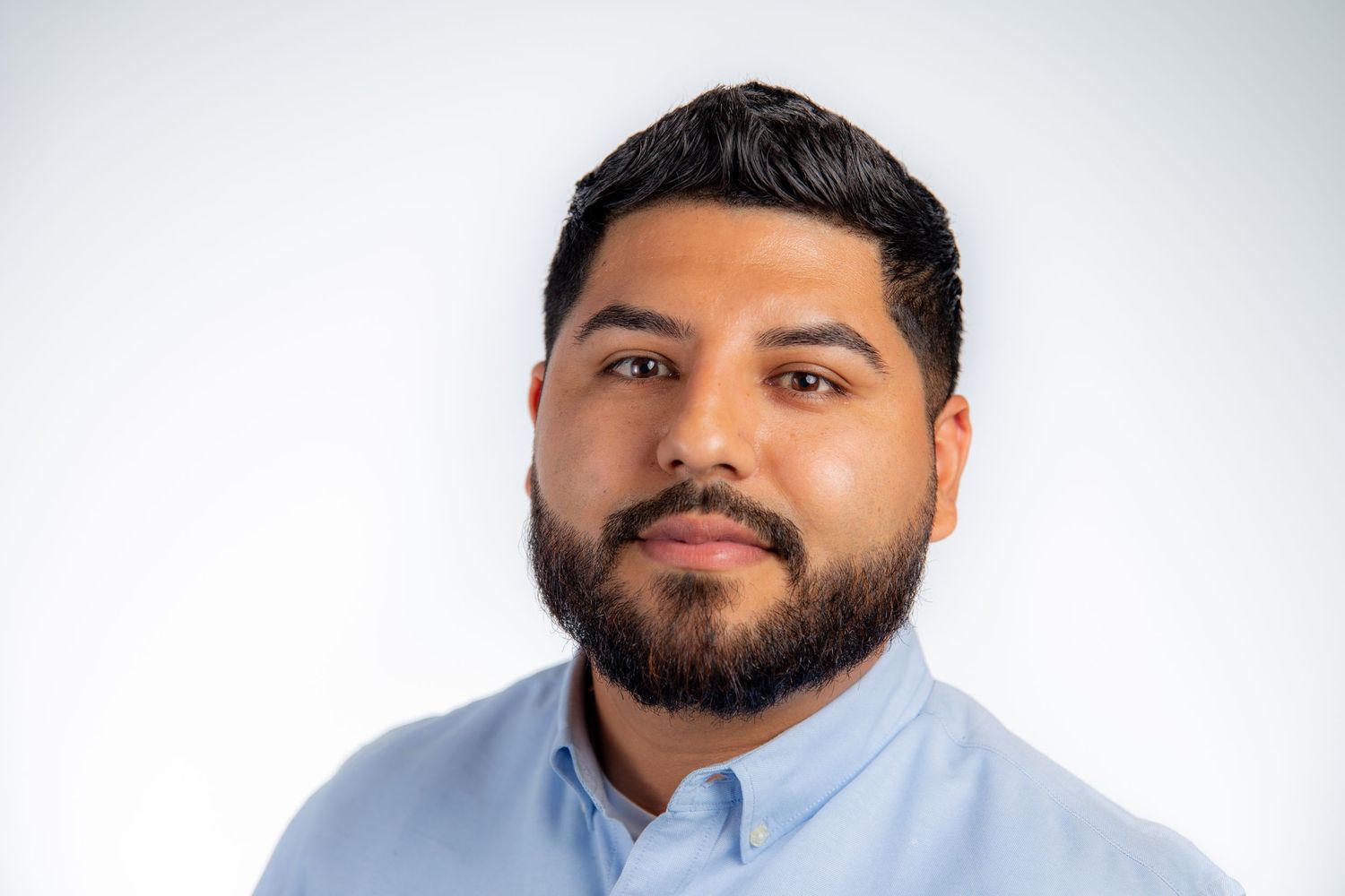 Professional headshot of a young bearded man in a light blue shirt against a clean white background.
