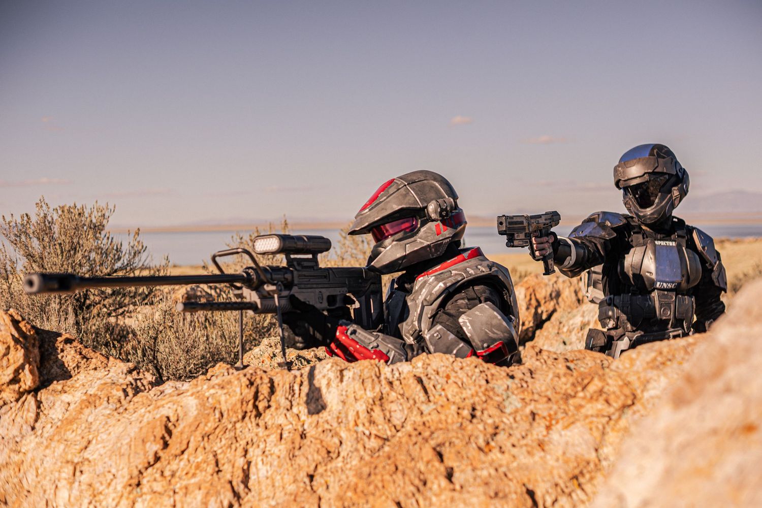 Two armored Halo ODST cosplayers take tactical positions behind rocky outcrop with rifles.