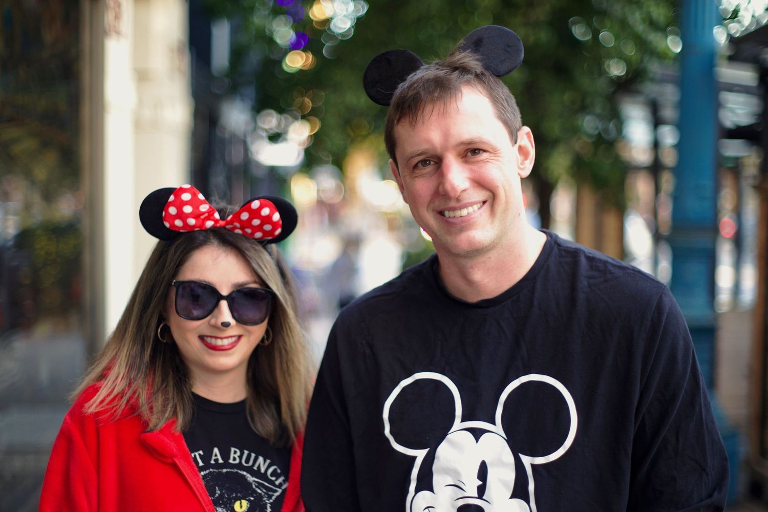Couple wearing Mickey and Minnie Mouse ears smiling together at a theme park outdoors.