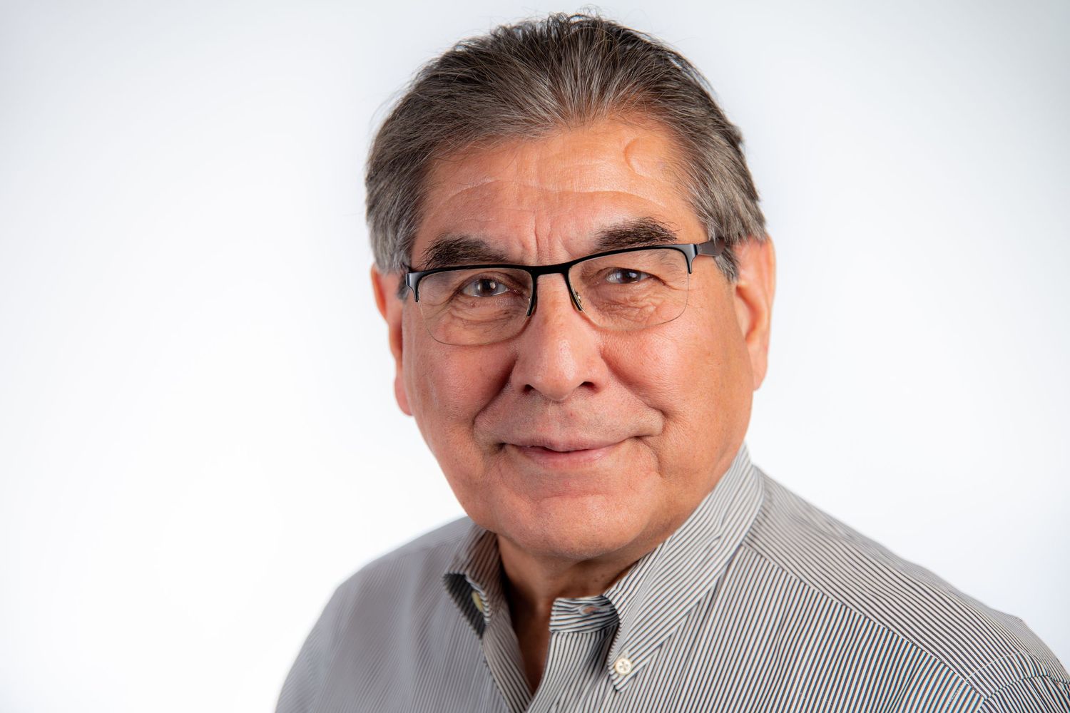Older man with glasses wearing a striped shirt smiling against a white background.