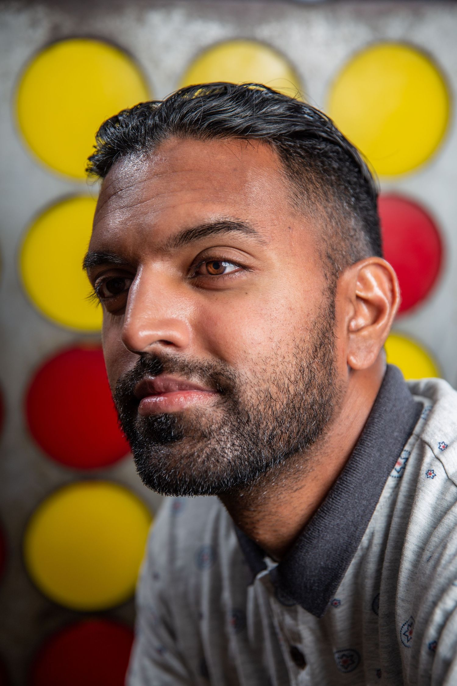 Bearded South Asian man with short dark hair posing against colorful red and yellow circle backdrop.