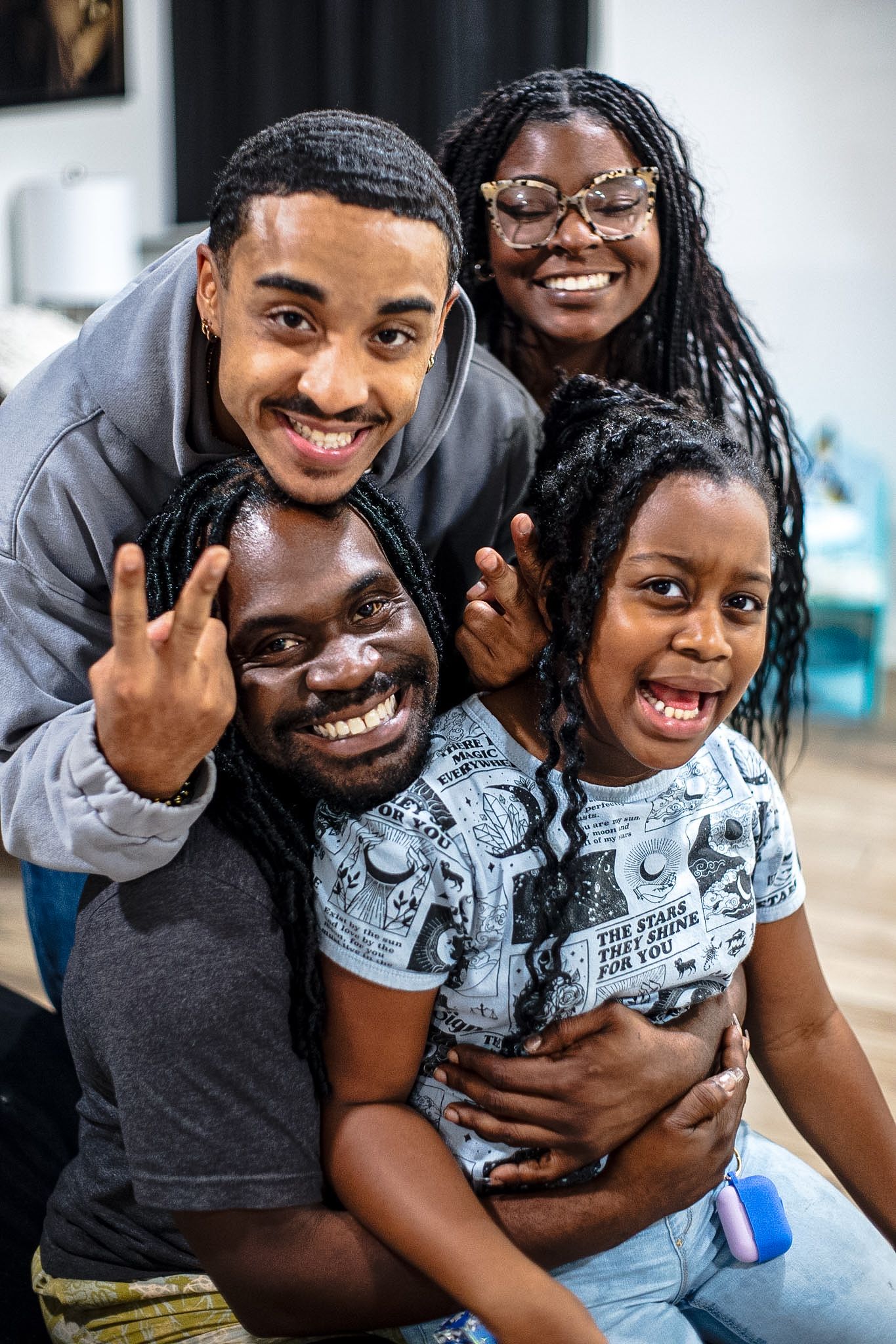 Happy Black family of four smiling and posing together indoors, making peace signs in a joyful portrait.