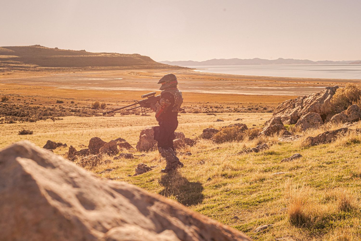 Halo ODST cosplayer in full armor stands silhouetted against golden desert landscape at sunset.
