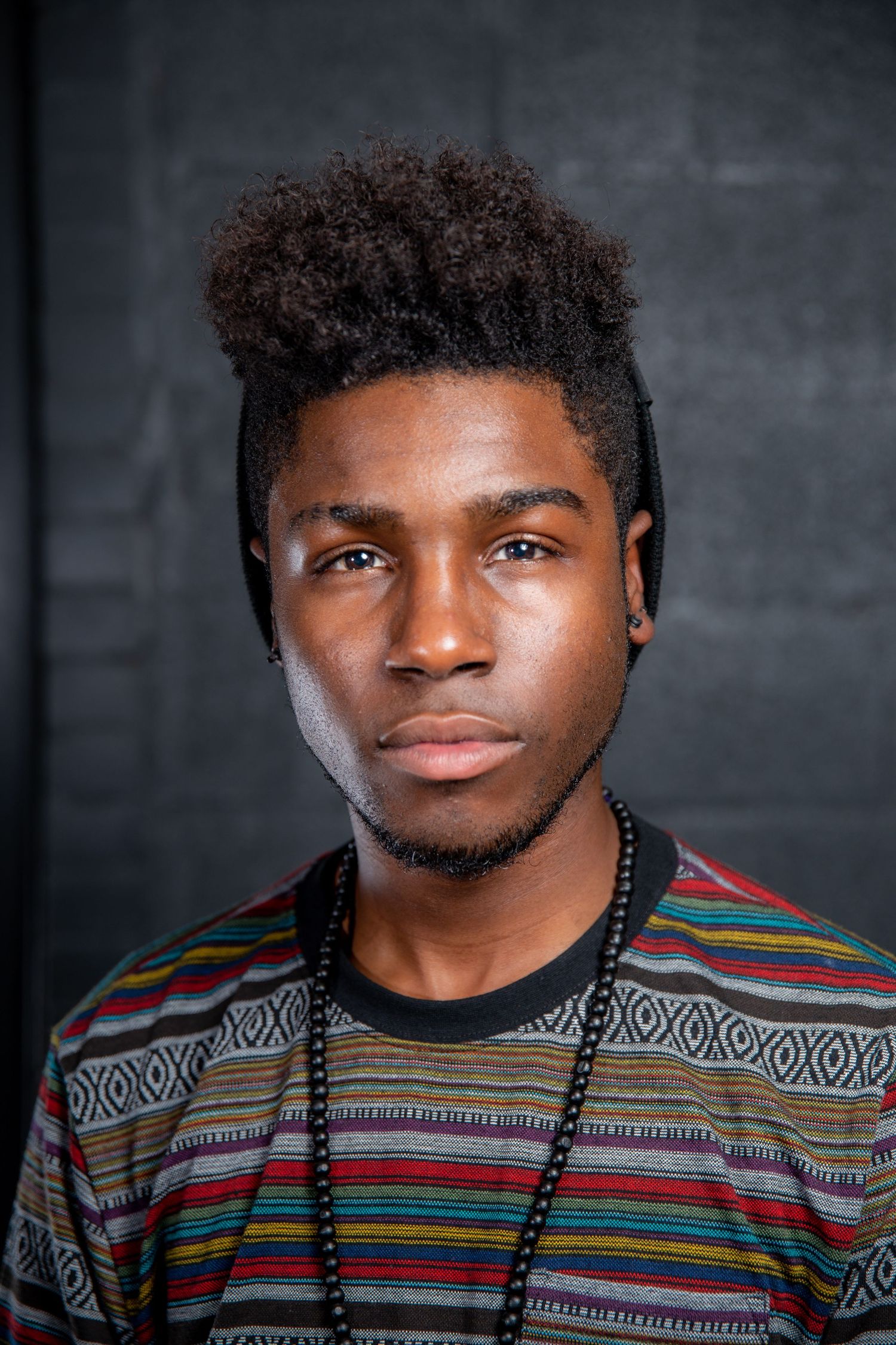Young Black man with stylish afro wearing a striped shirt and beaded necklace.
