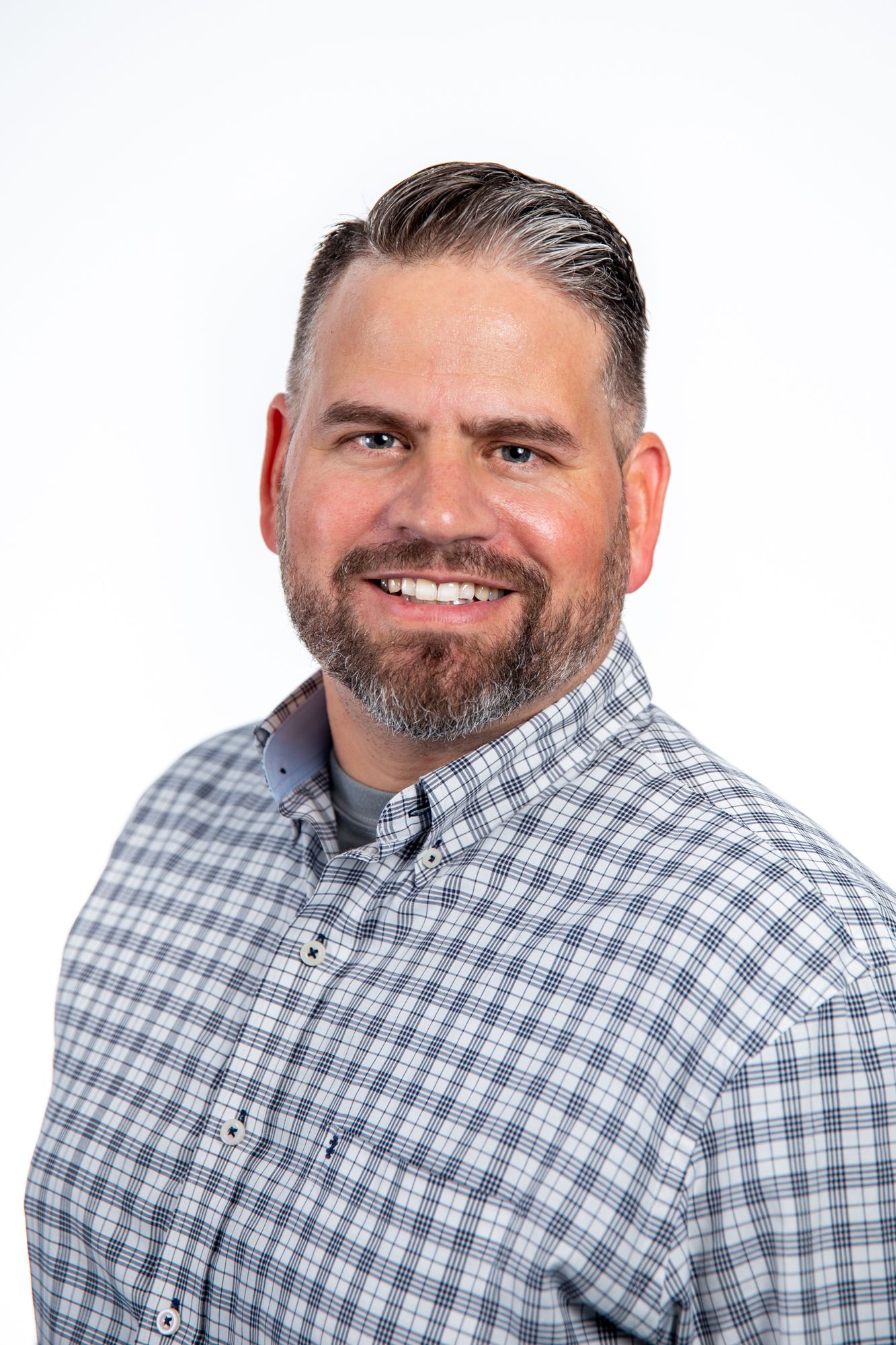 Smiling bearded man in plaid shirt poses for professional headshot on white background.