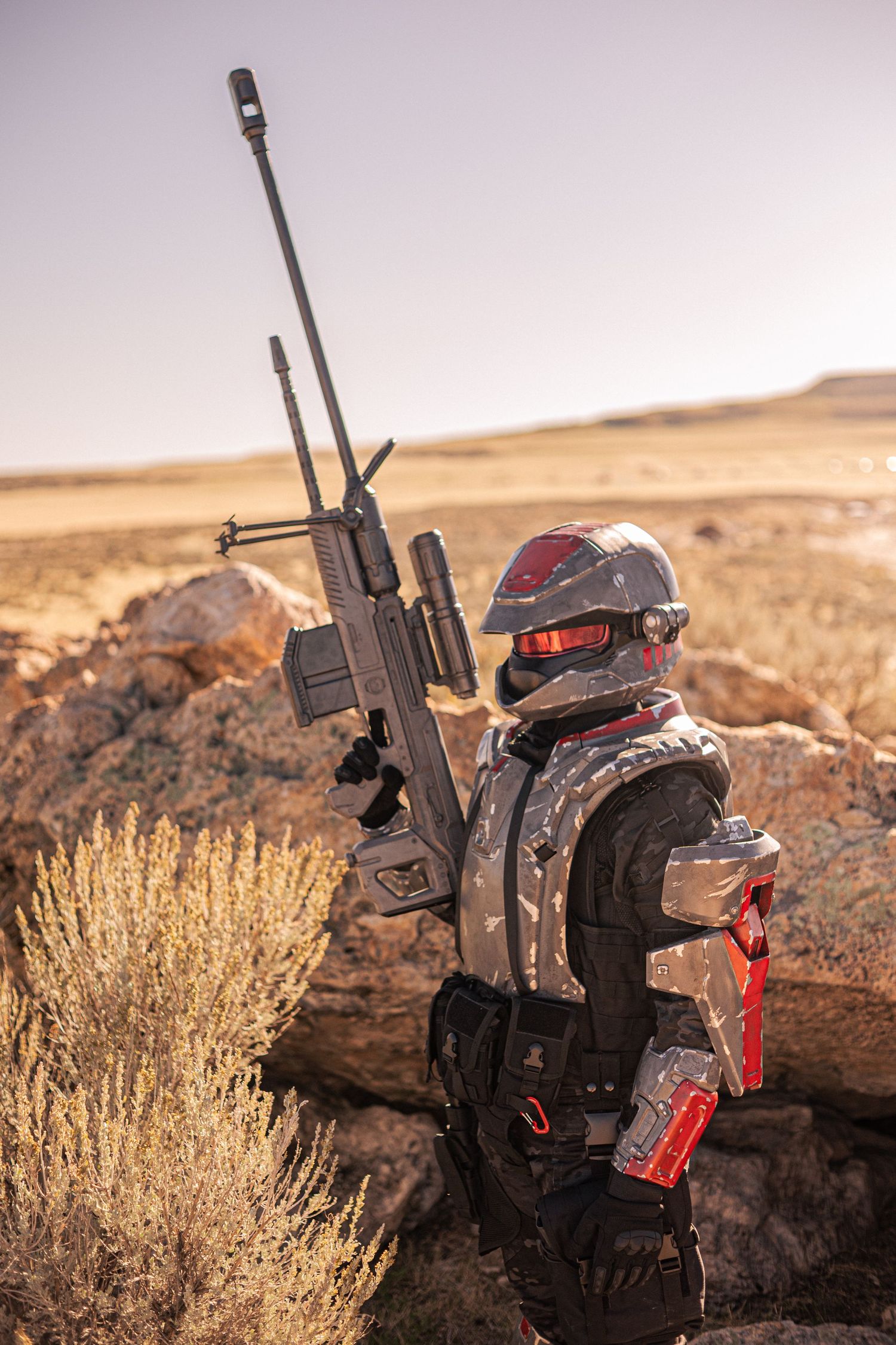 Futuristic soldier in sci-fi armor holding sniper rifle in desert landscape cosplay.