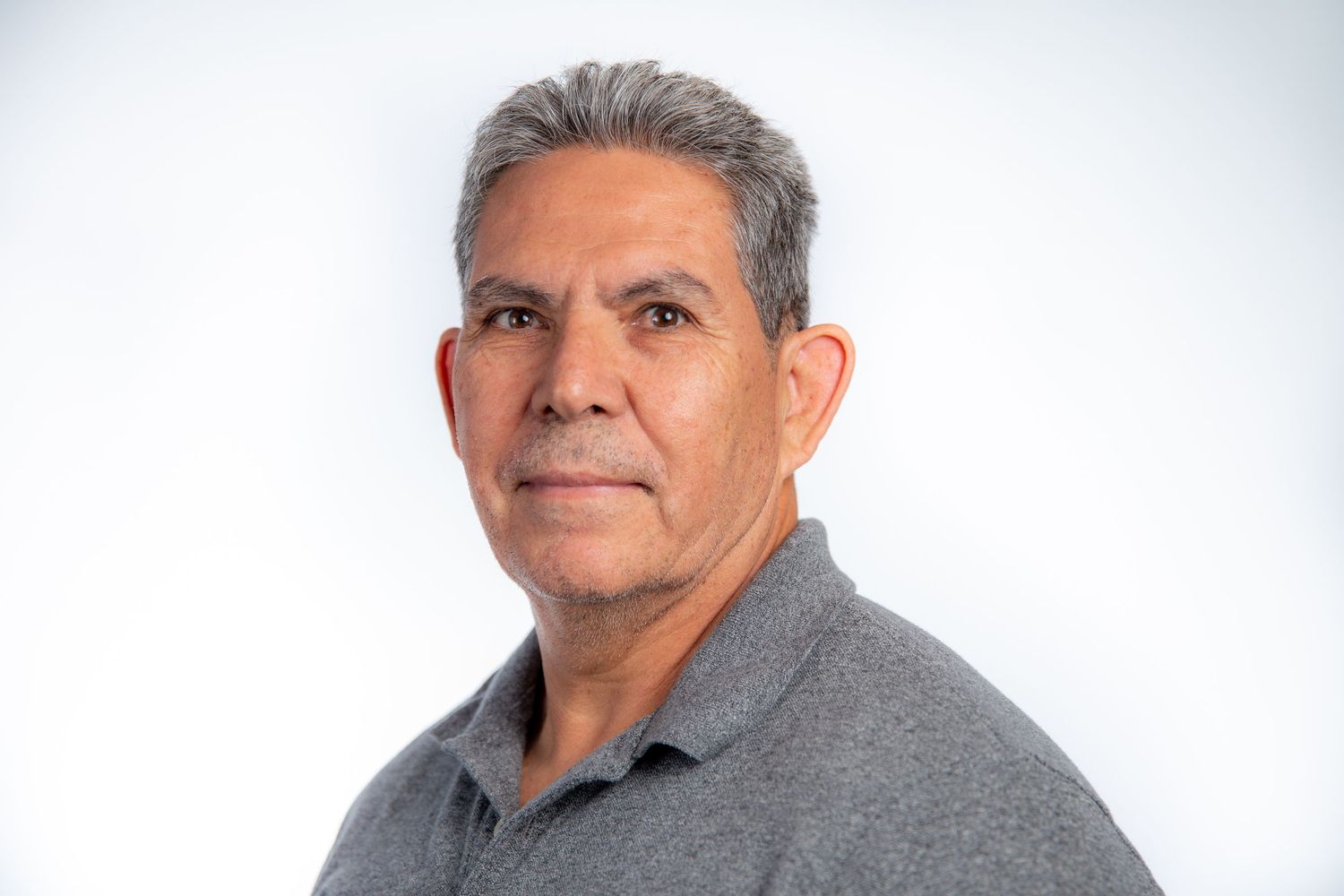 Middle-aged man in a gray polo shirt posing for a professional headshot against a white background.