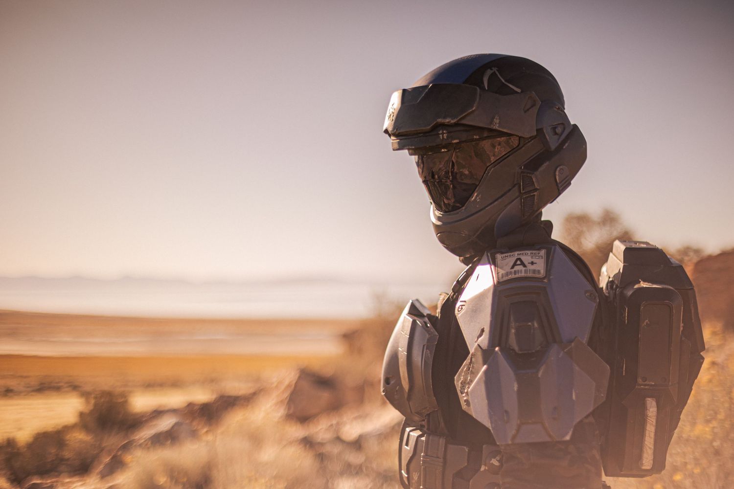 Close-up of a person wearing a sleek futuristic sci-fi helmet and armor suit in a desert landscape.