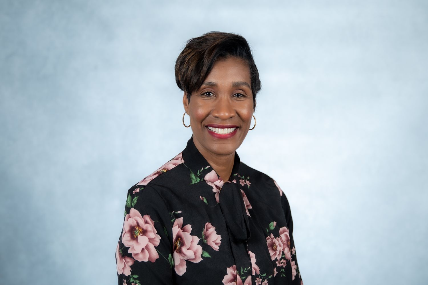 Smiling Black woman in floral blouse with short hair poses for professional headshot.
