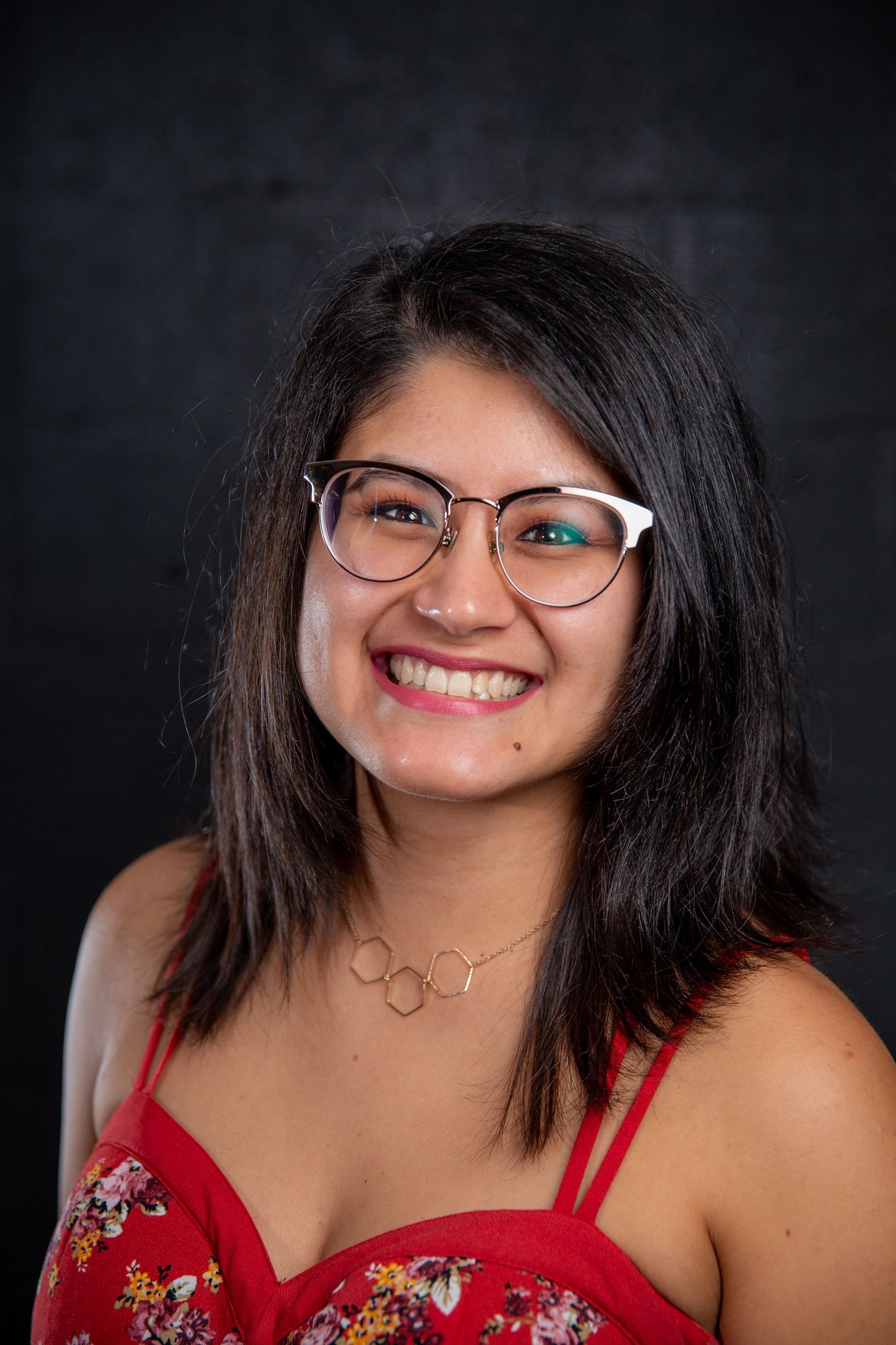 Smiling young woman with glasses and dark hair wearing a red floral top.