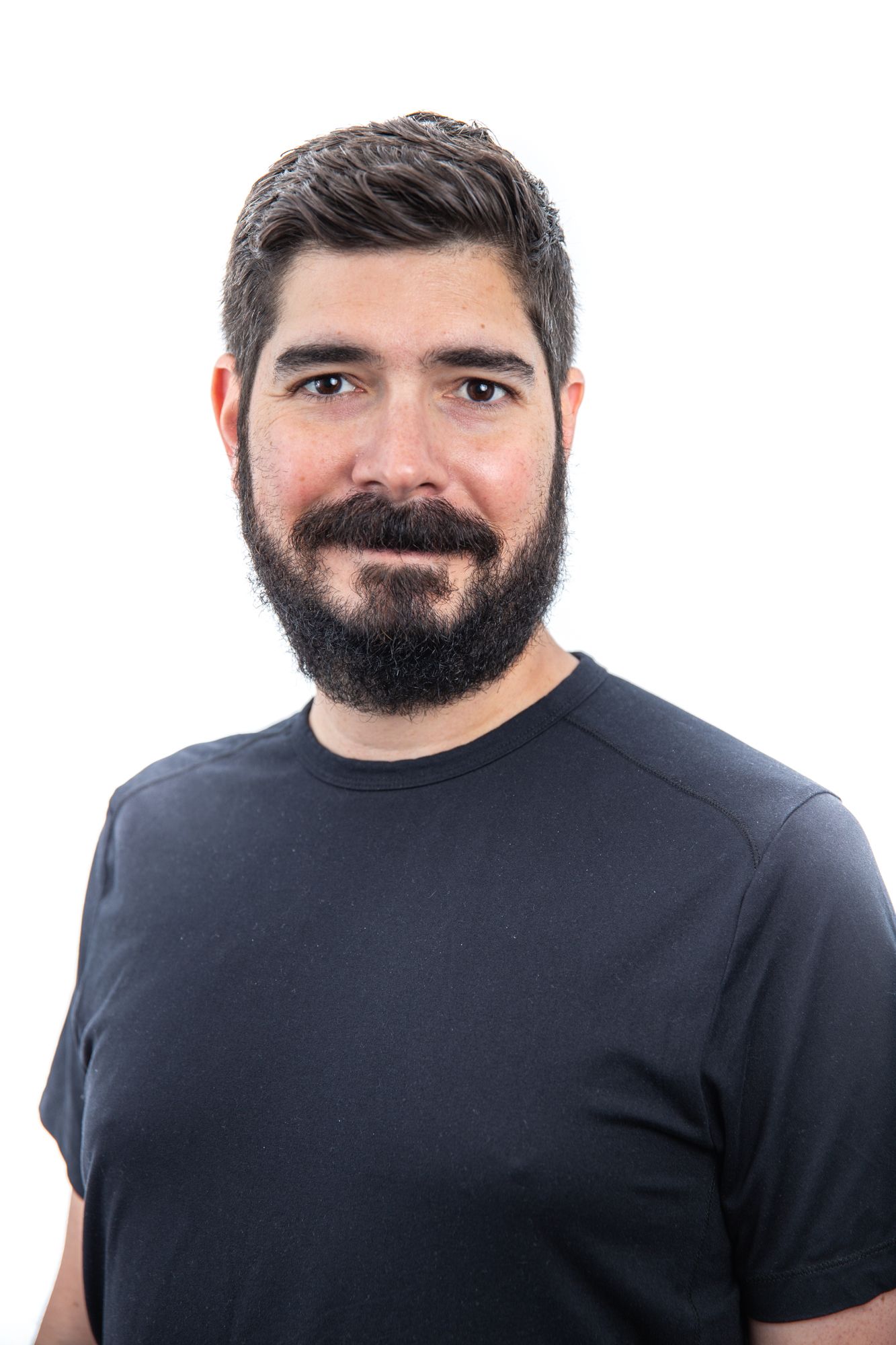 Man with dark hair and beard wearing a black t-shirt, professional headshot on white background.
